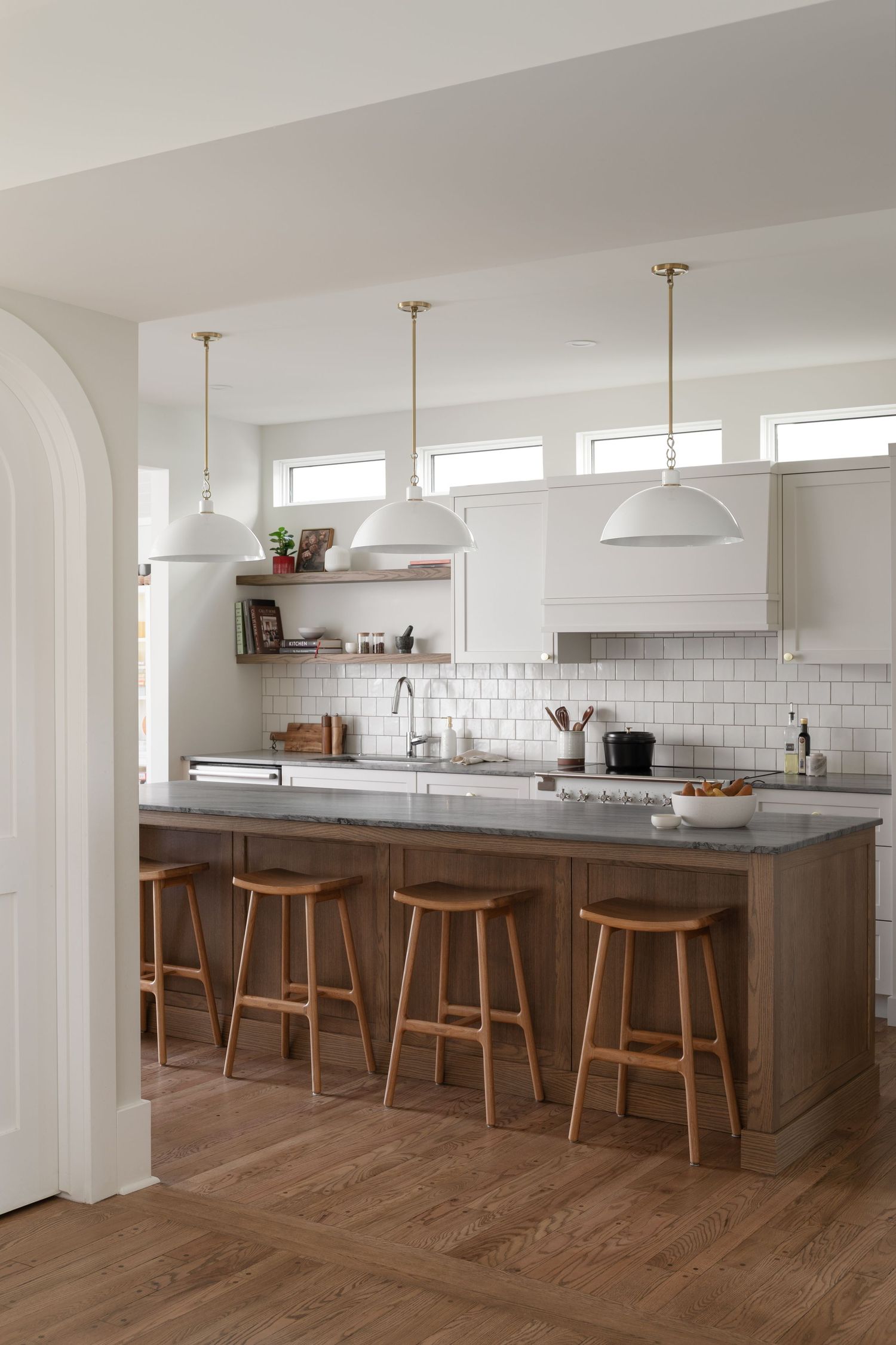 Modern kitchen with white cabinets, subway tile backsplash, gray island, wooden barstools, and pendant lights.