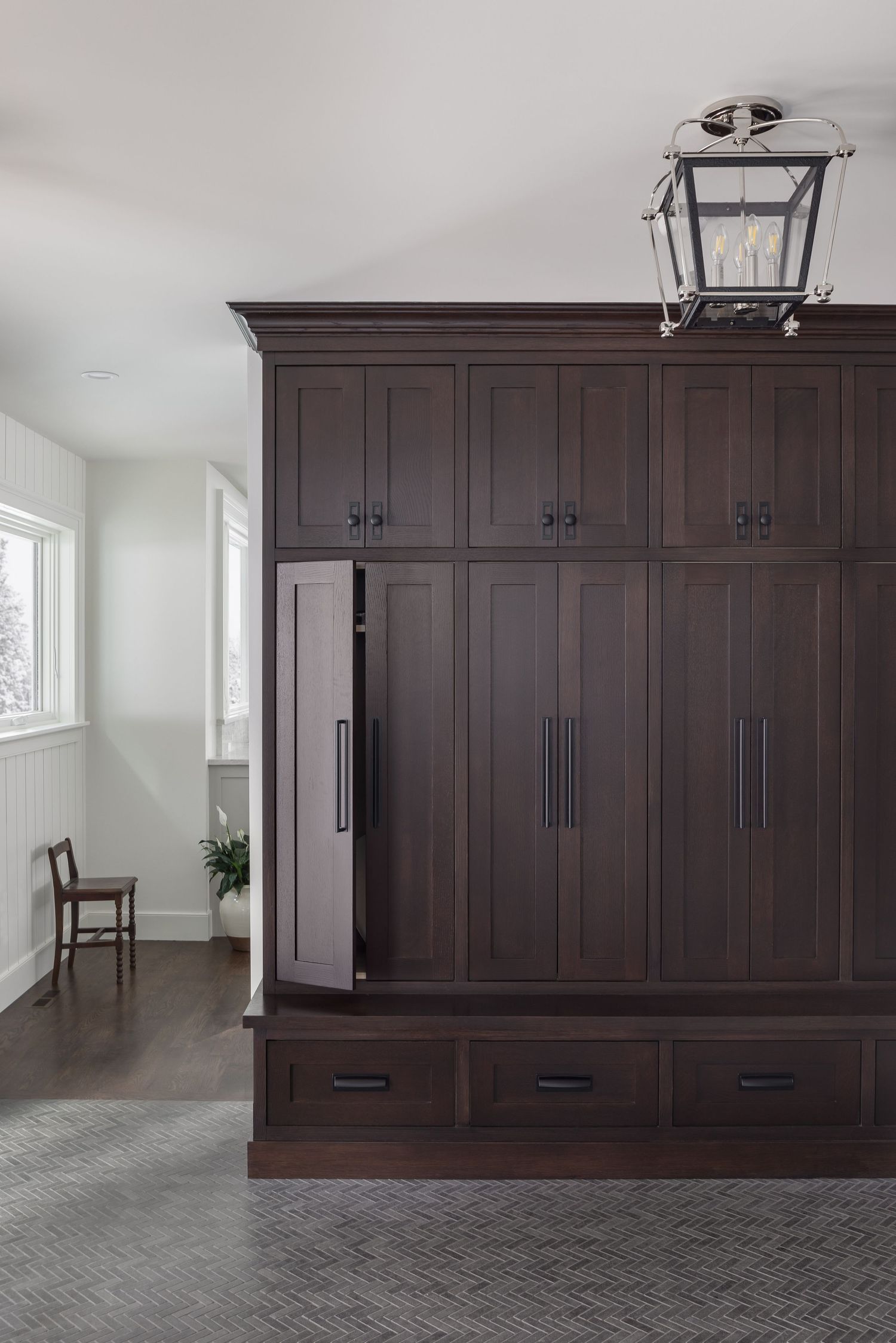 Dark espresso built-in mudroom lockers with black hardware, bottom drawers, and nickel lantern ceiling light.