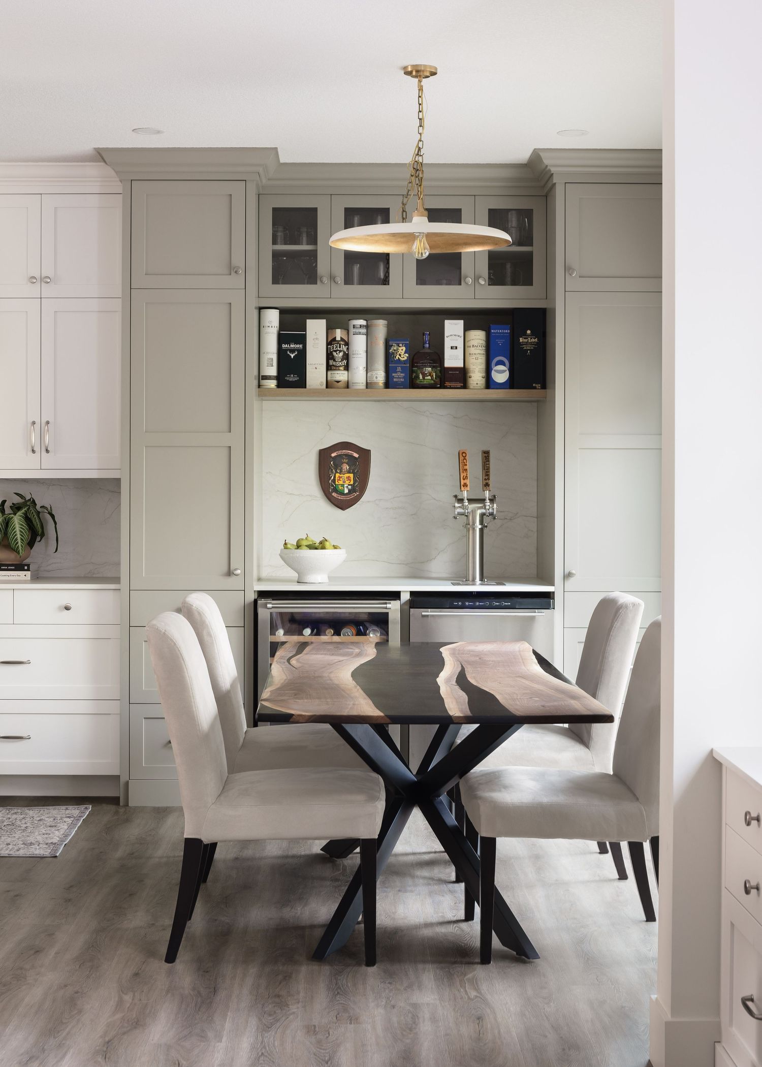 Elegant dining nook with sage green built-in cabinets, live-edge table, draft beer taps, and gold pendant light.