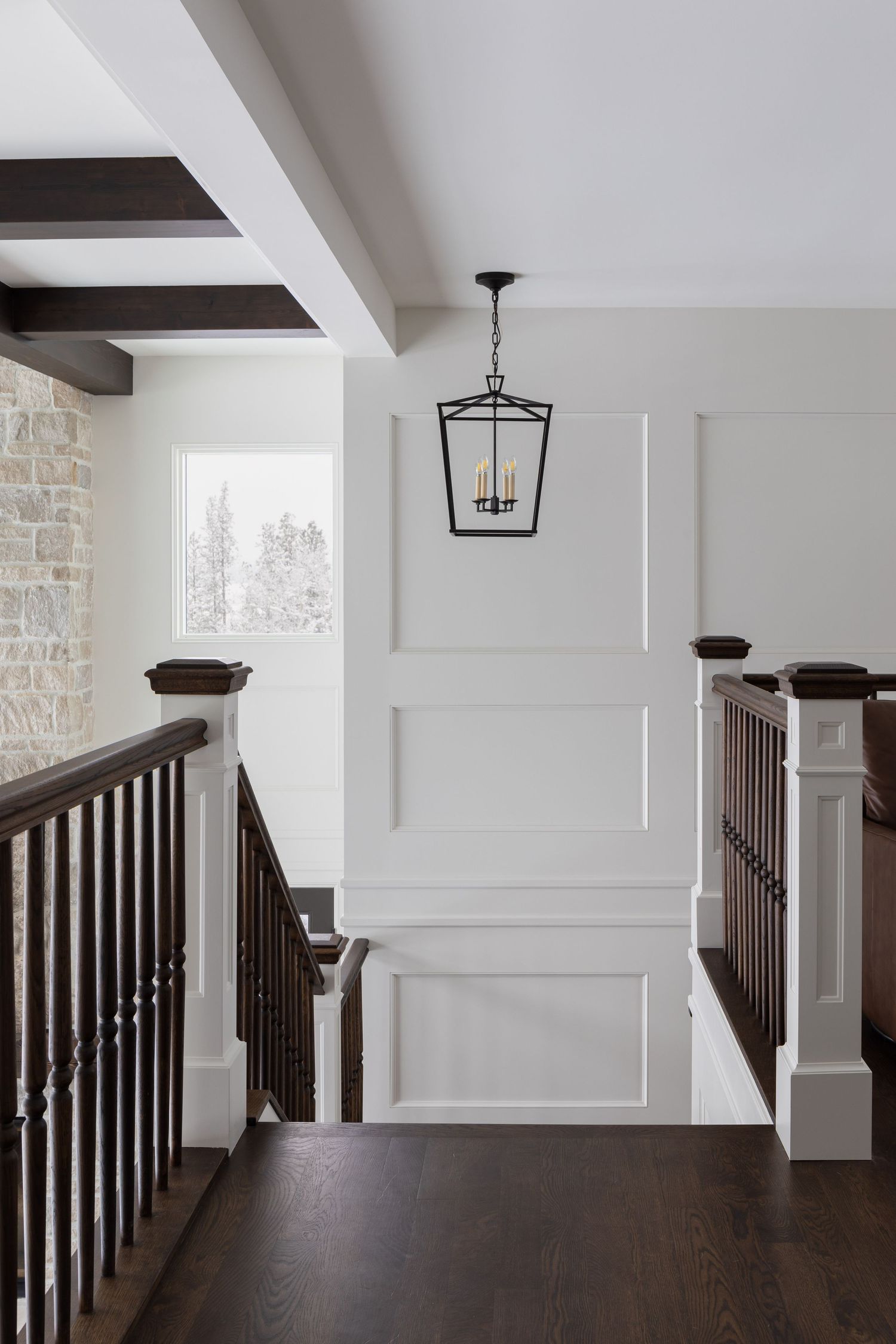 Traditional staircase landing with dark wood railings, white wainscoting panels, and black lantern pendant light.
