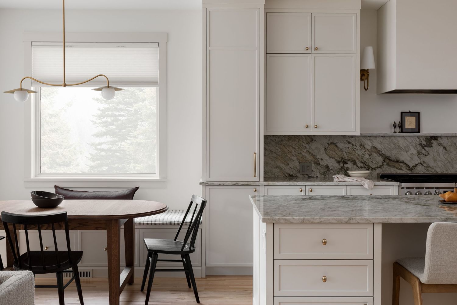 Open-concept kitchen and dining area with marble countertops, white cabinets, and natural wood round table.
