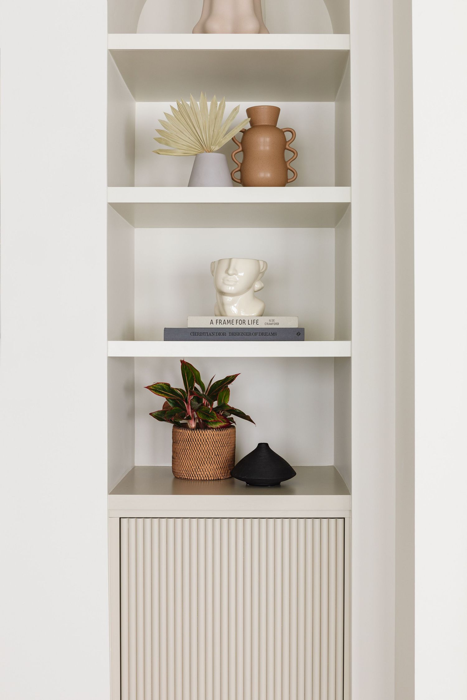 White built-in shelving unit with ceramic vases, face sculpture, plant, and ribbed cabinet.