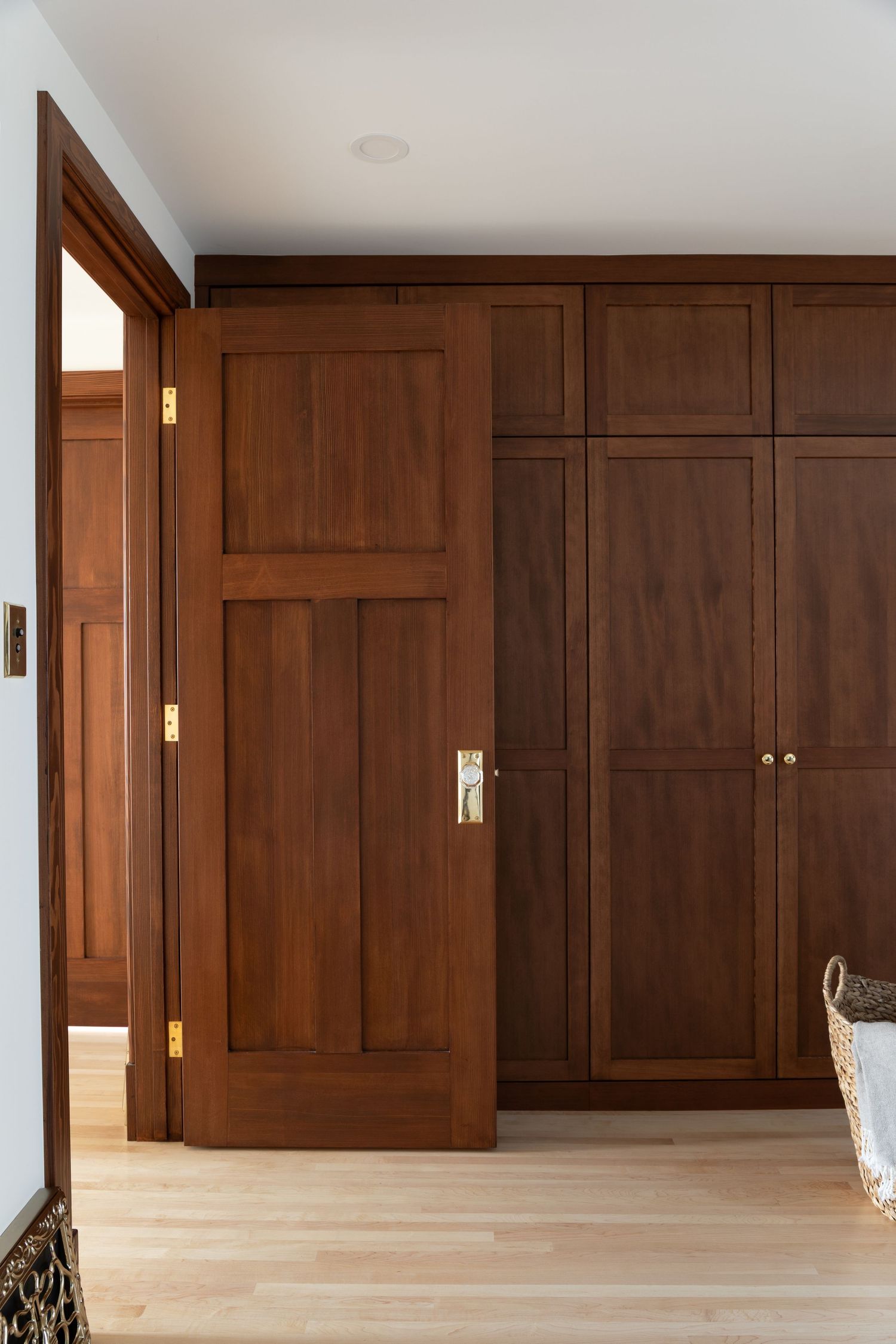 Dark walnut built-in wardrobe with brass hardware and matching interior door on light hardwood floors.
