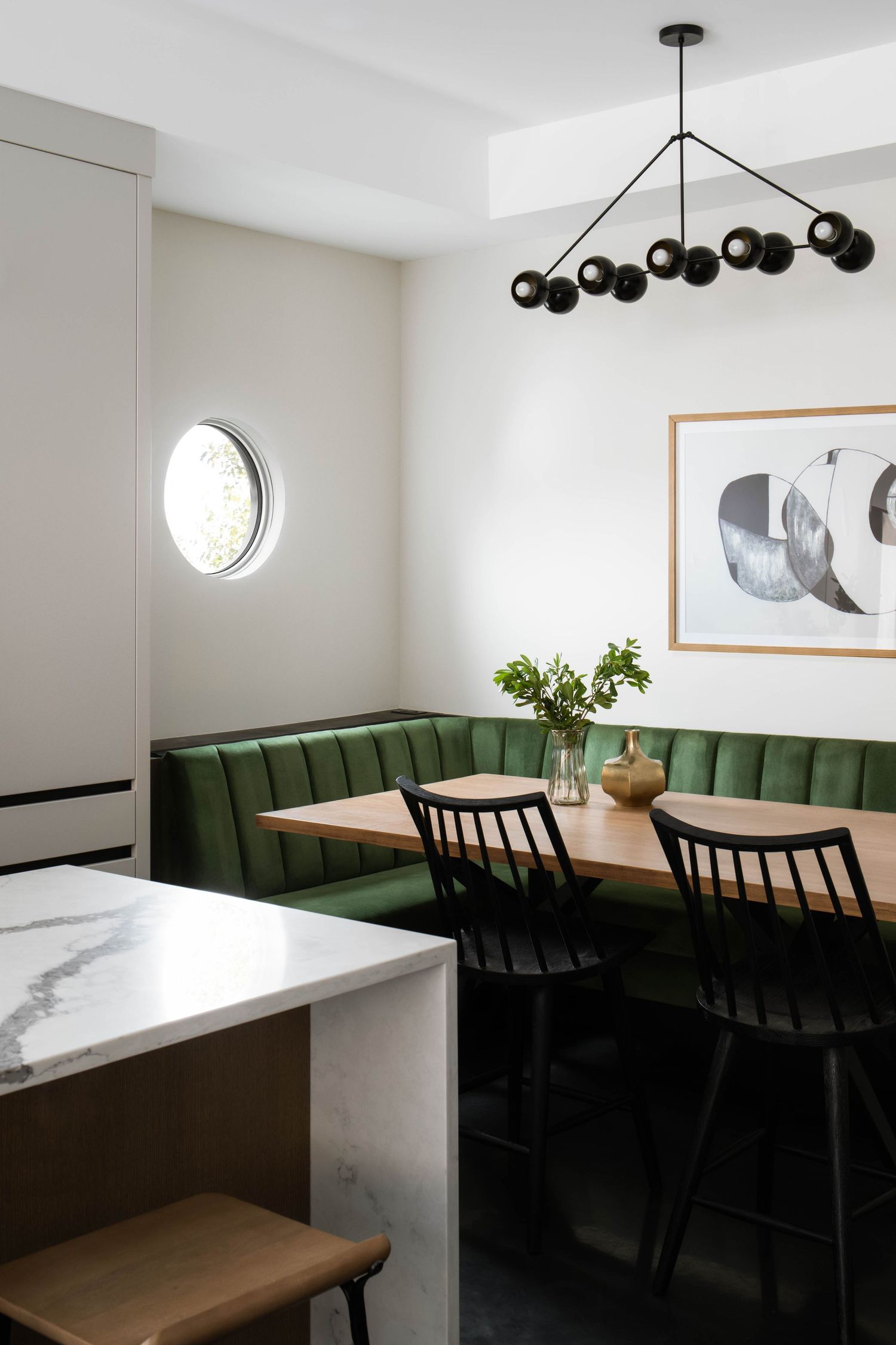 Modern dining nook with green velvet banquette, black chairs, wood table, and sculptural black globe chandelier.