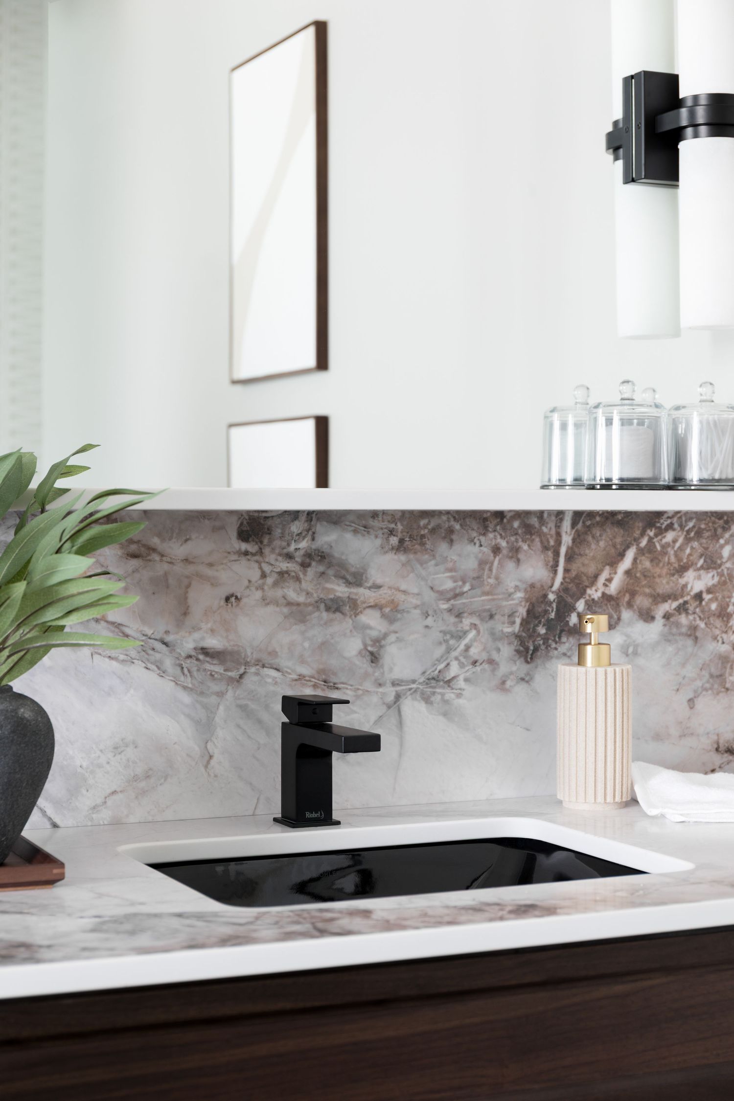 Elegant bathroom vanity with black undermount sink, marble backsplash, dark wood cabinets, and gold soap dispenser.