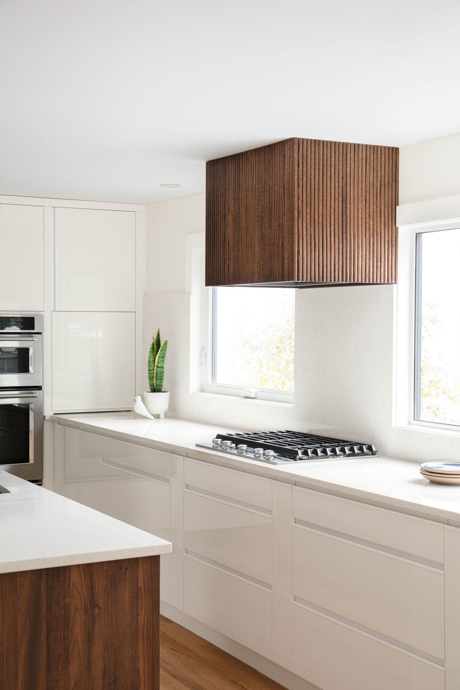 Modern white kitchen with reeded walnut range hood, handleless cabinets, and wood island accent.