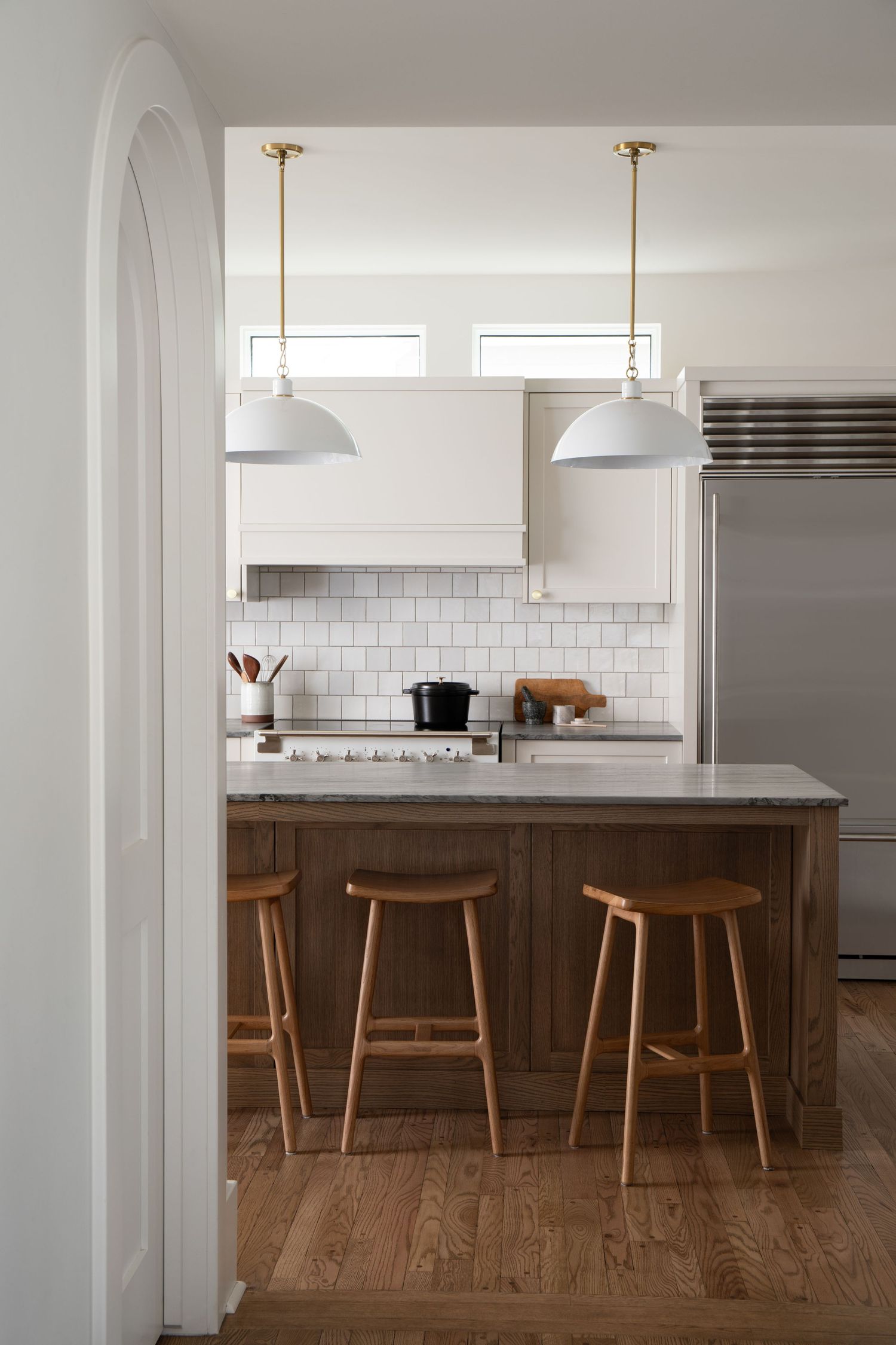 Modern kitchen with white cabinets, subway tile backsplash, wood island, bar stools, and brass pendant lights.