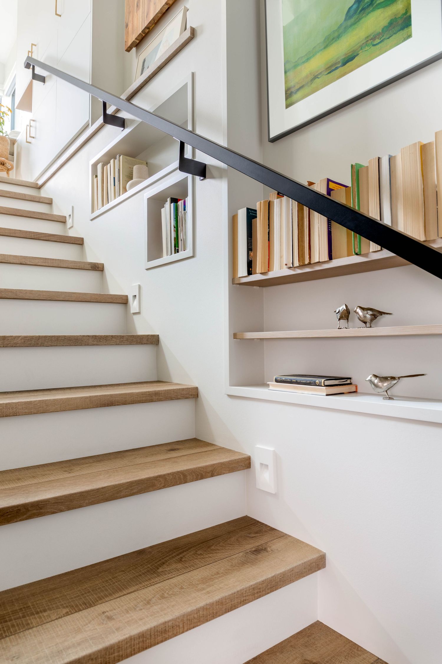 Modern staircase with wood treads, black railing, and built-in wall bookshelves.
