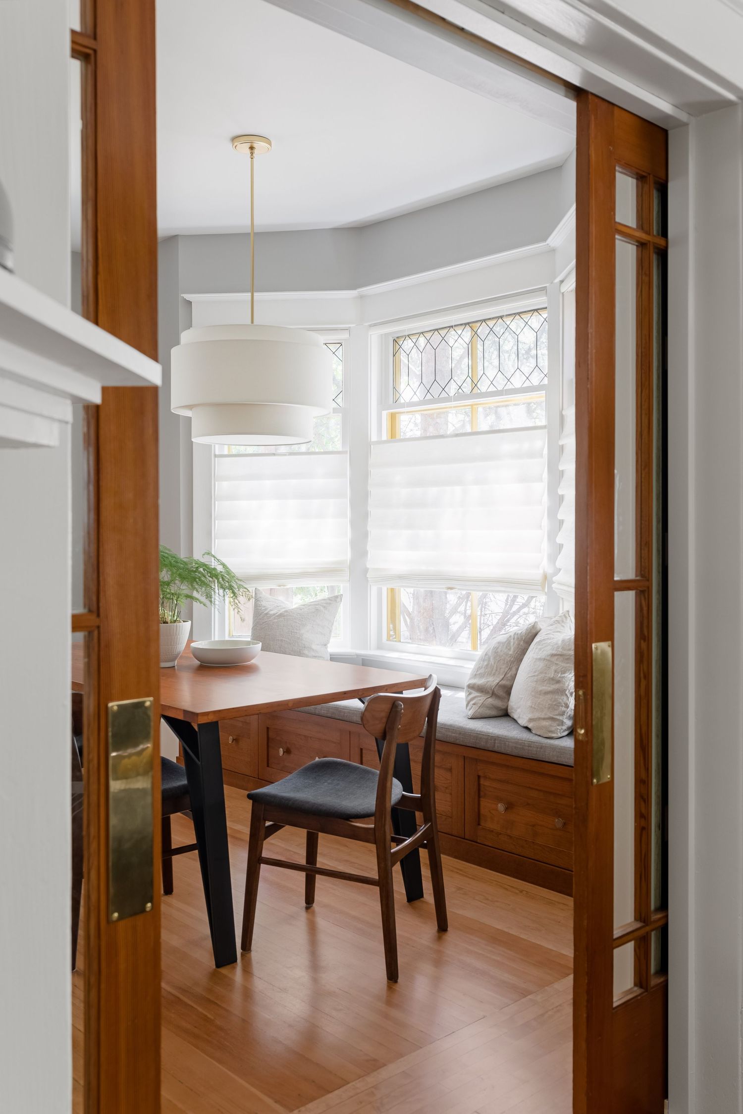 Cozy breakfast nook with round wood table, vintage chairs, bay window, and sliding barn doors.