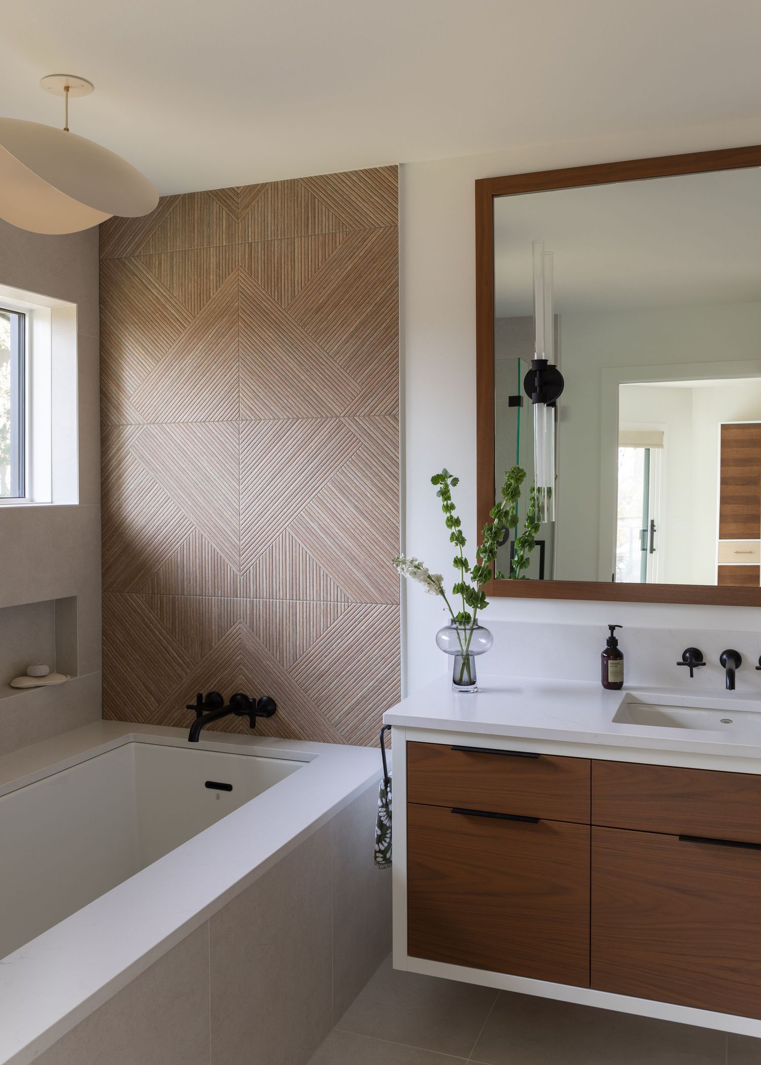 Contemporary bathroom with herringbone wood-look accent wall, freestanding tub, floating walnut vanity, and large mirror.