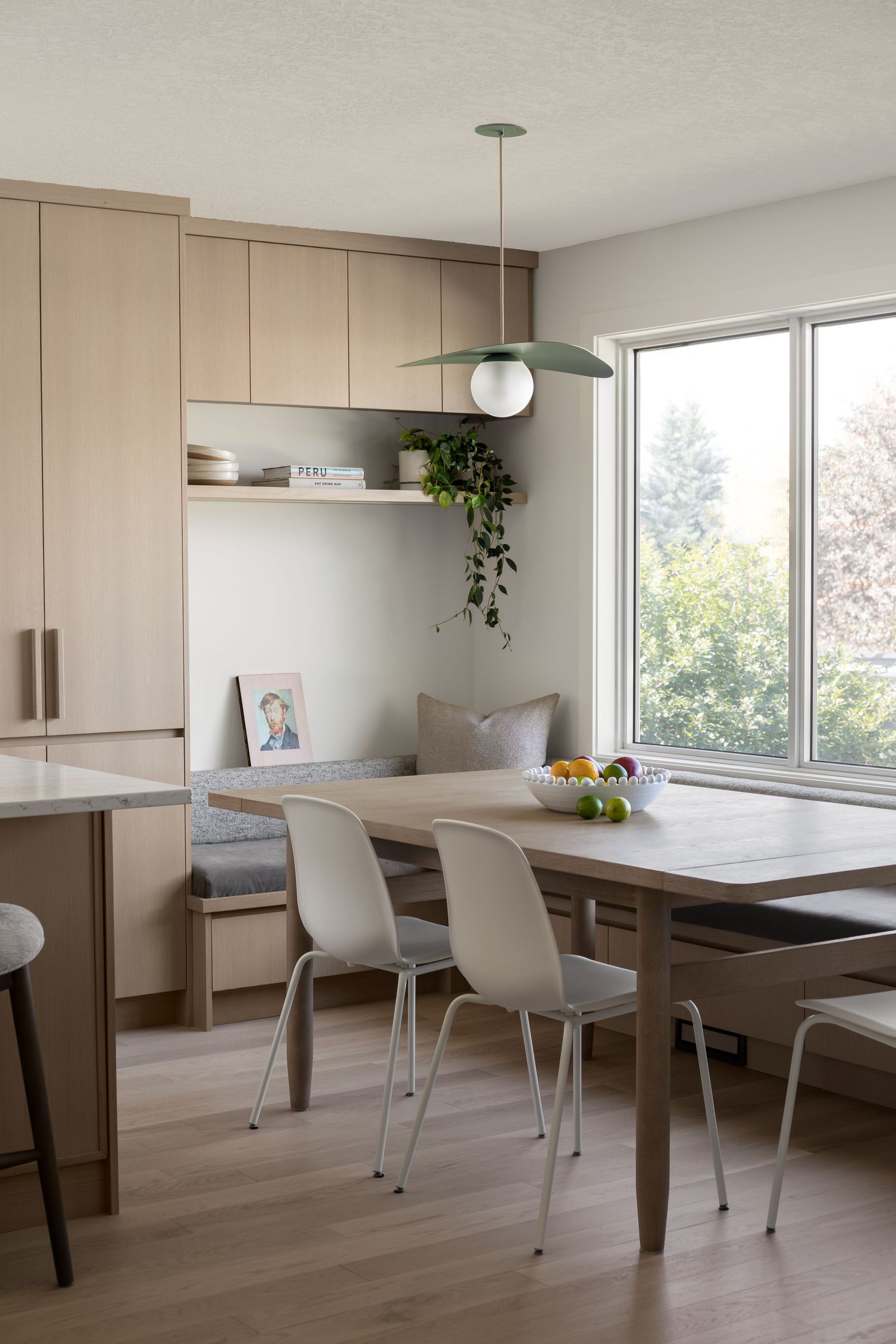 Scandinavian dining area with light wood table, white chairs, green pendant light, and window seat.