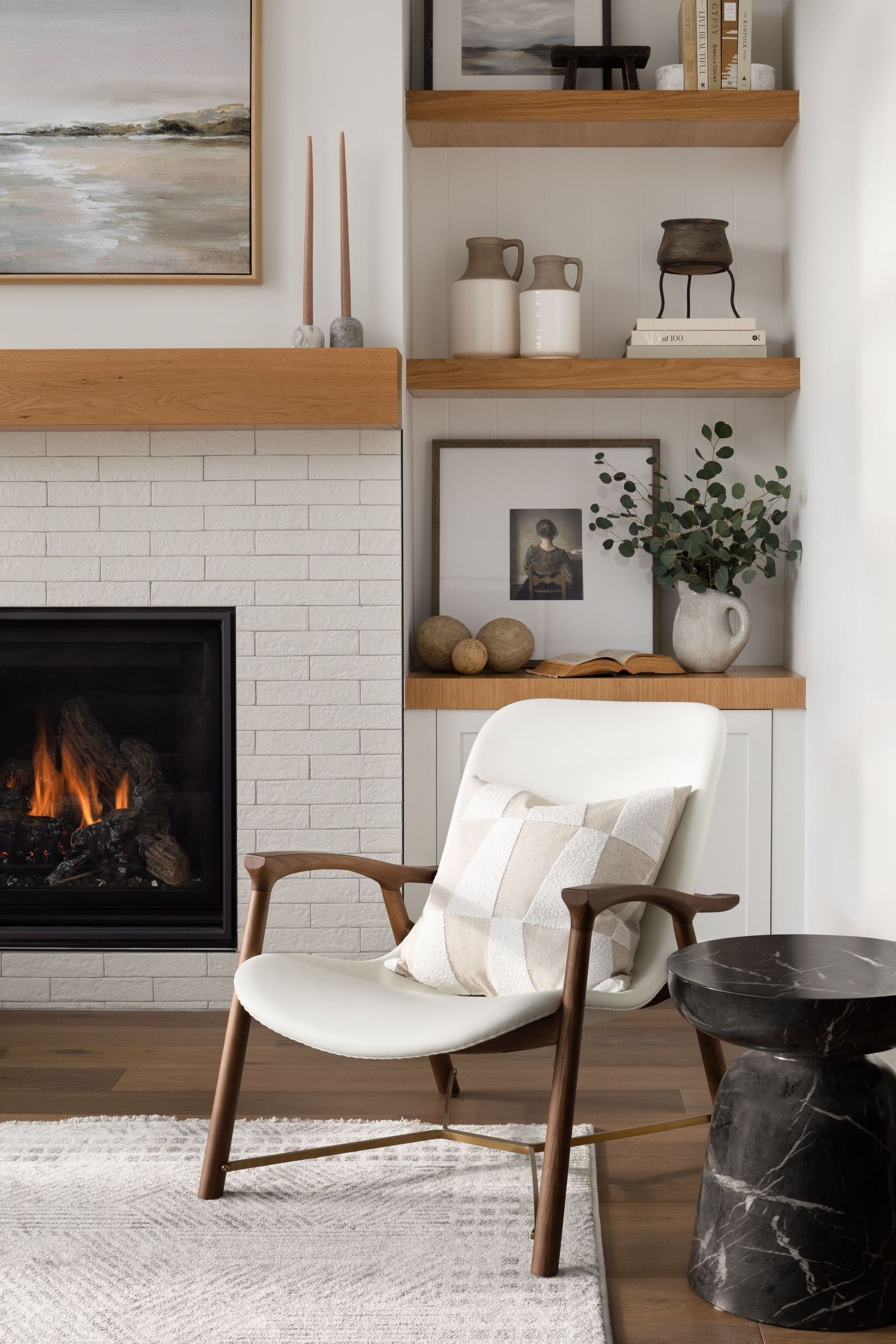 Cozy living room nook with white brick fireplace, oak shelves, and white accent chair.