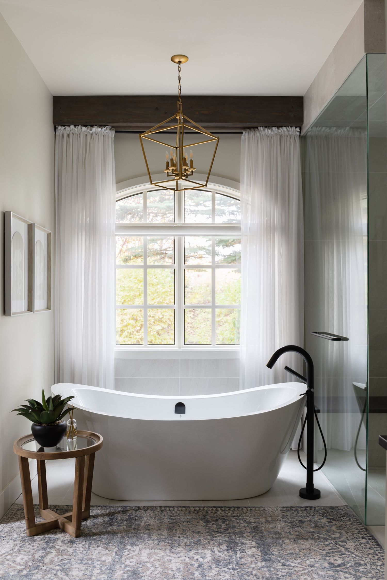 Elegant bathroom with freestanding soaking tub, black floor-mount faucet, brass lantern pendant, arched window, and patterned tile.