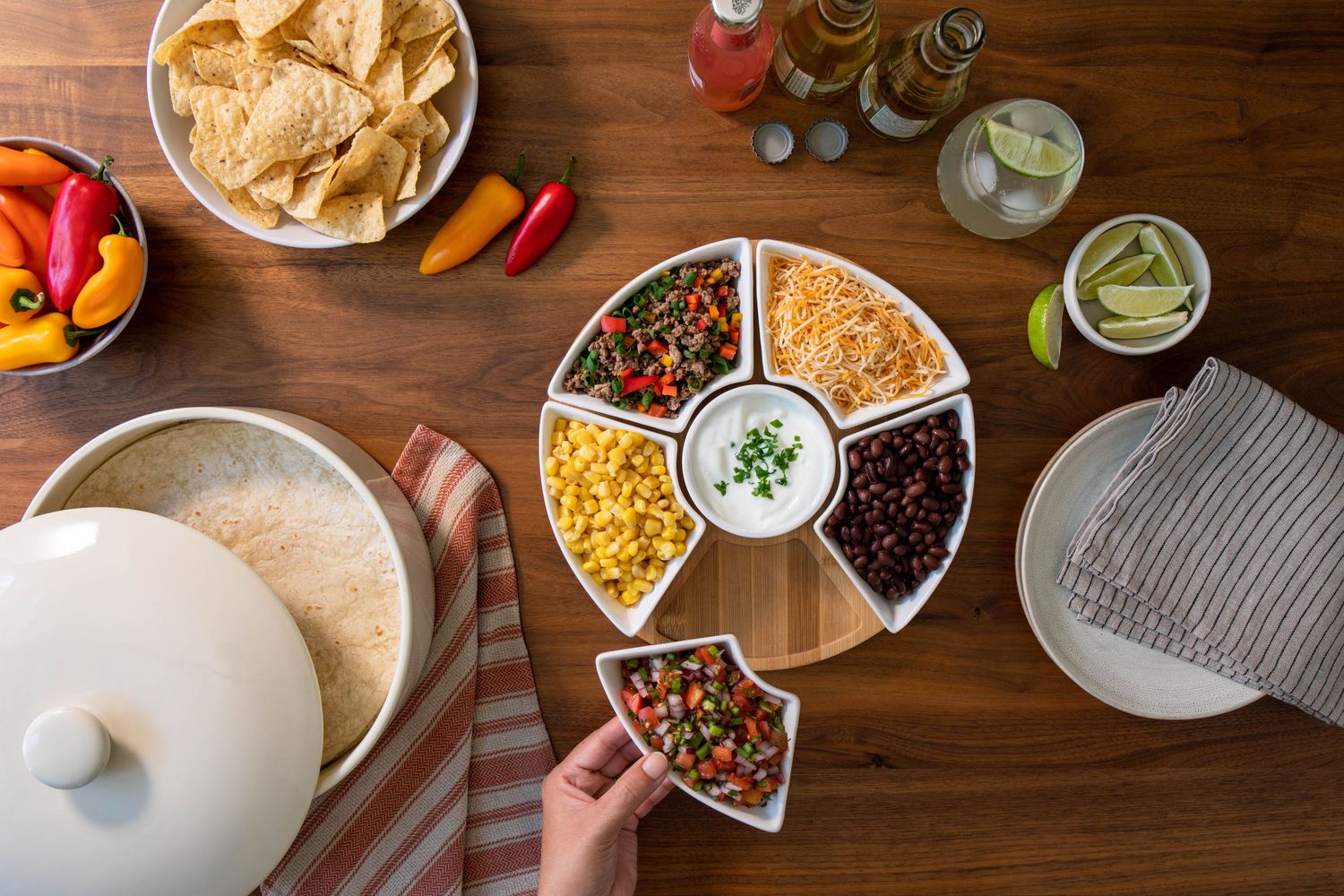 Overhead view of a taco night spread with a divided condiment tray, chips, tortillas, and drinks.