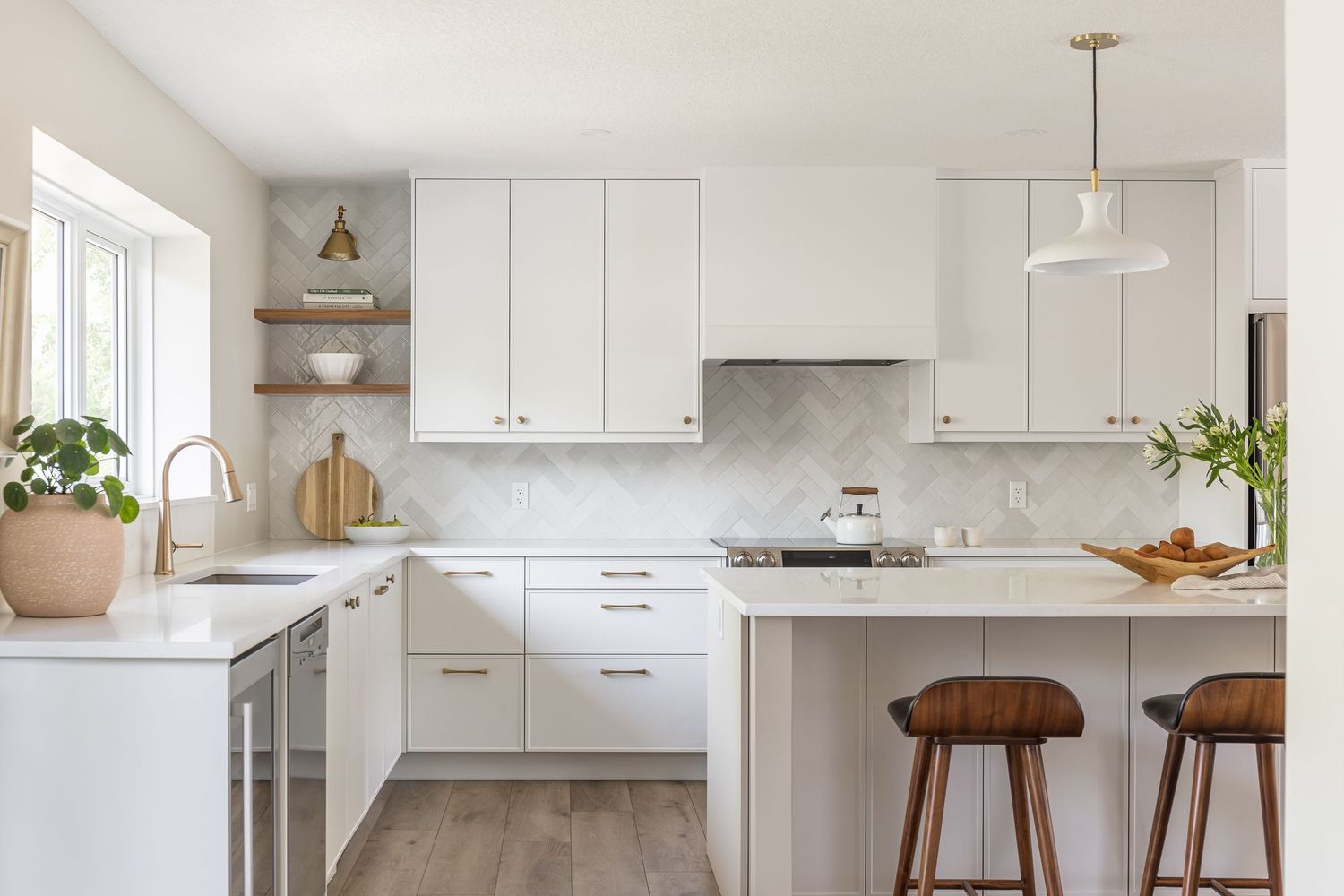 White shaker kitchen with herringbone marble backsplash, open shelving, island with bar stools, and pendant lighting.