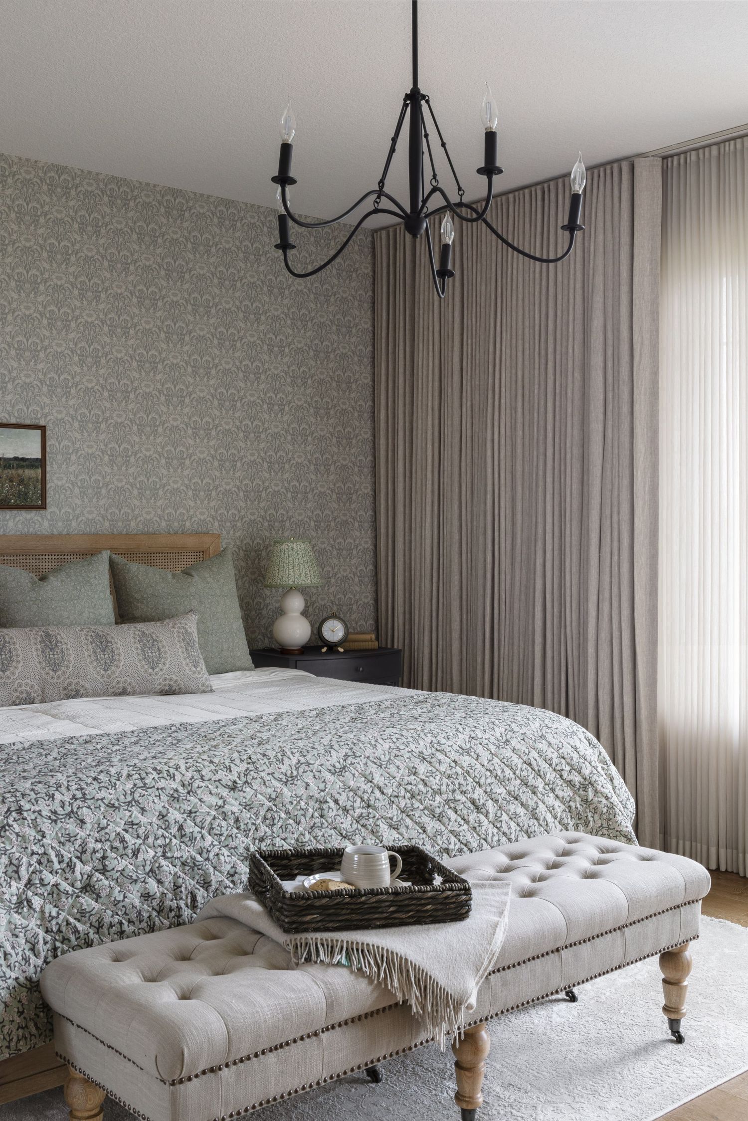 Elegant bedroom with sage green wallpaper, tufted bench, chandelier, and layered neutral bedding.