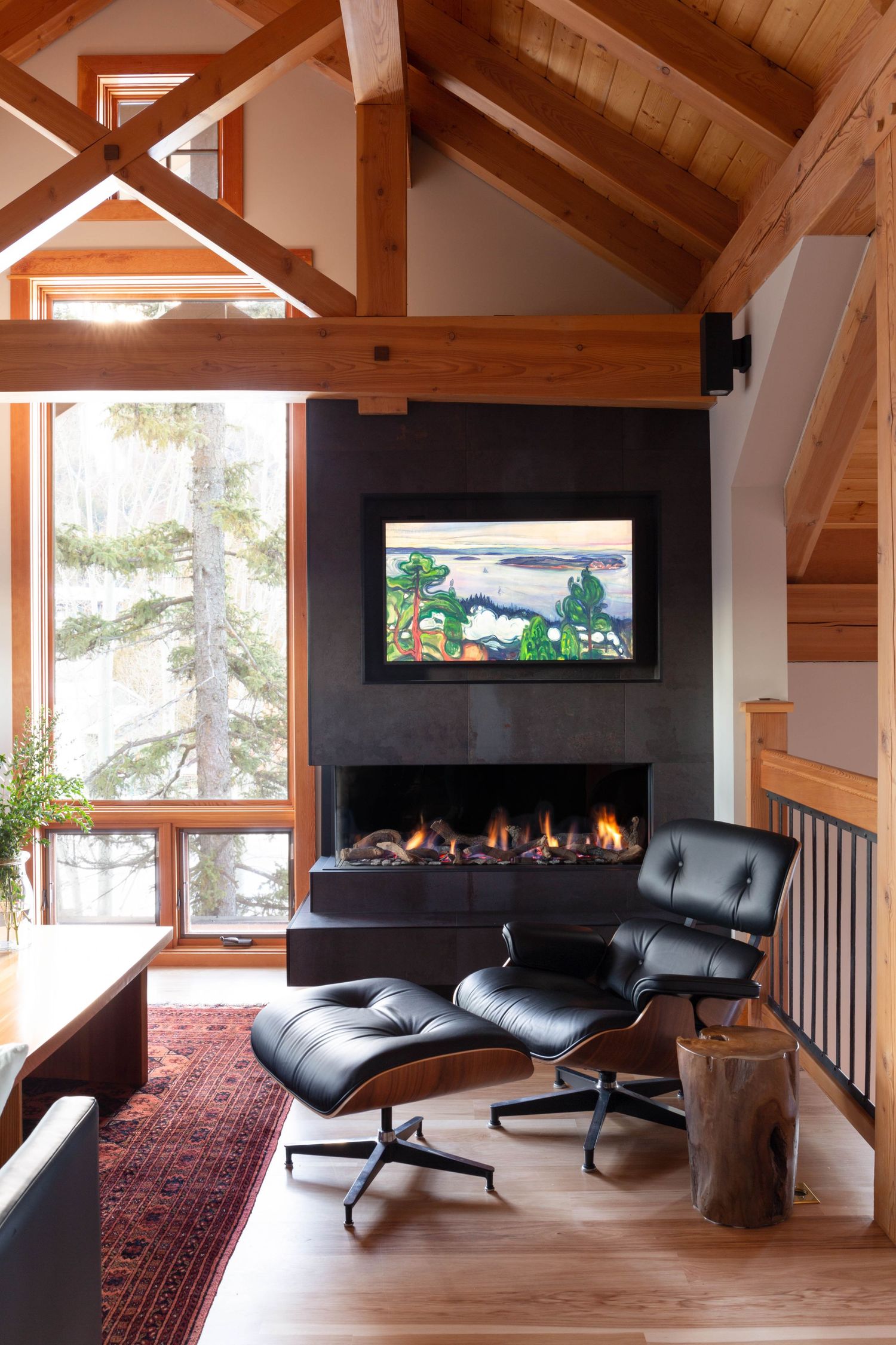 Rustic cabin living room with vaulted wood ceiling, black fireplace, Eames lounge chair, and TV.