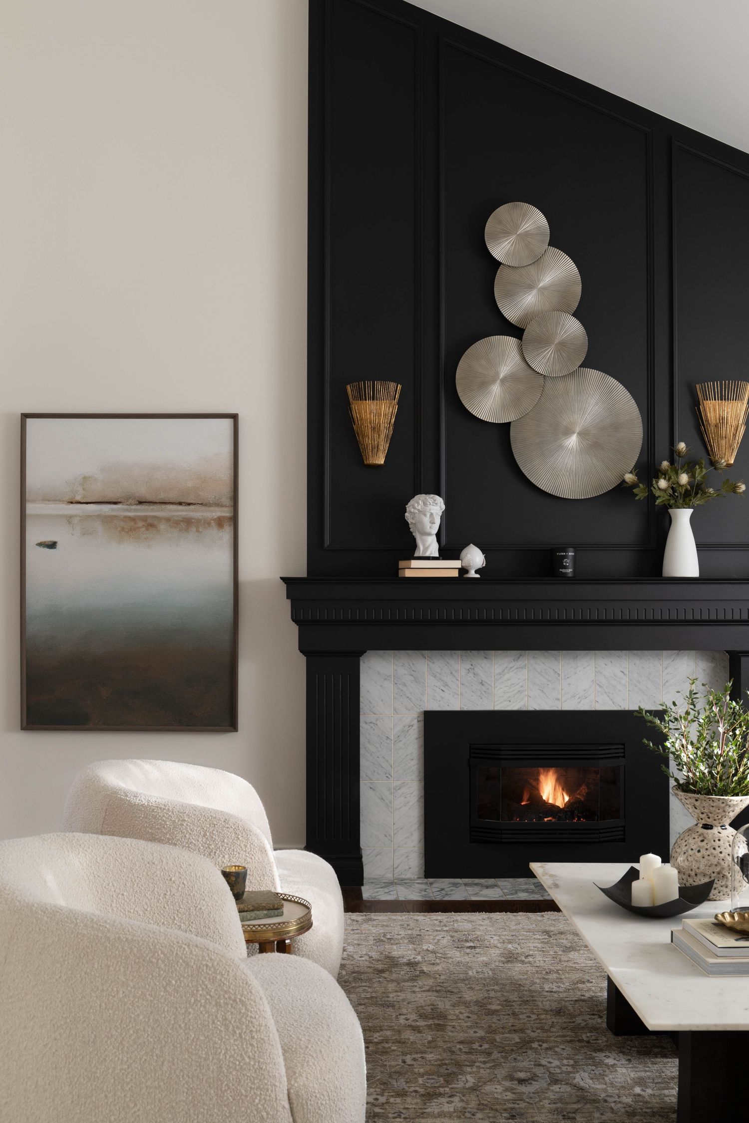 Elegant living room with black accent wall, marble fireplace, metallic disc wall art, and cream bouclé chairs.