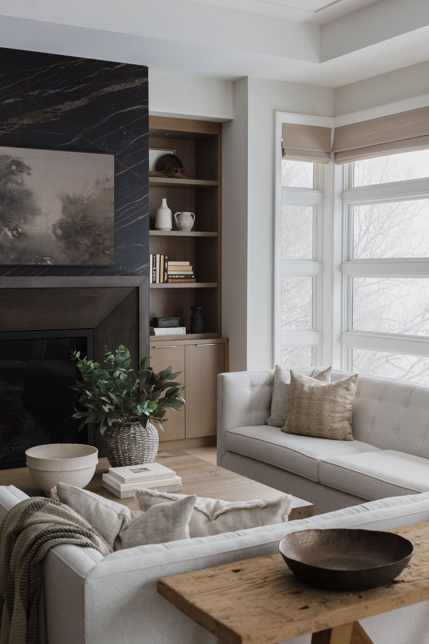 Bright living room with marble fireplace, built-in shelving, cream sofas, and woven roman shades.