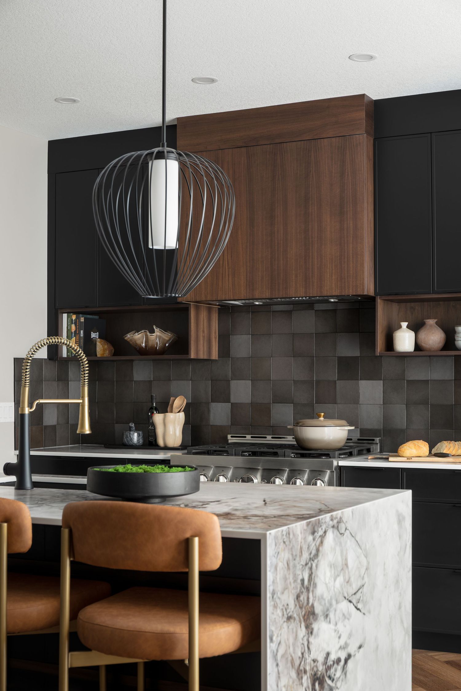 Luxury dark kitchen featuring marble island, walnut cabinets, black tile backsplash, and brass faucet.