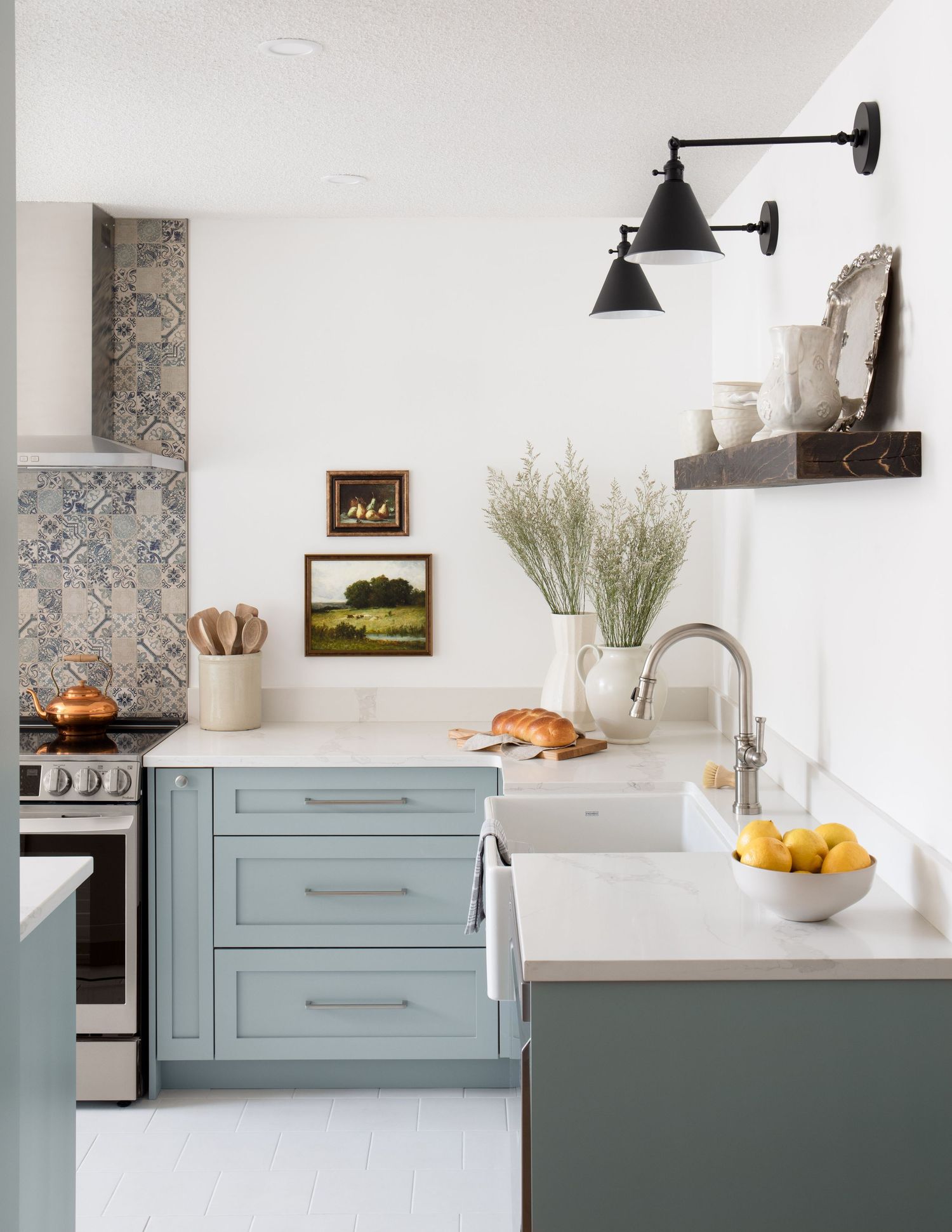 Sage green kitchen cabinets with white countertops, patterned tile backsplash, black sconce lights, and open shelving.