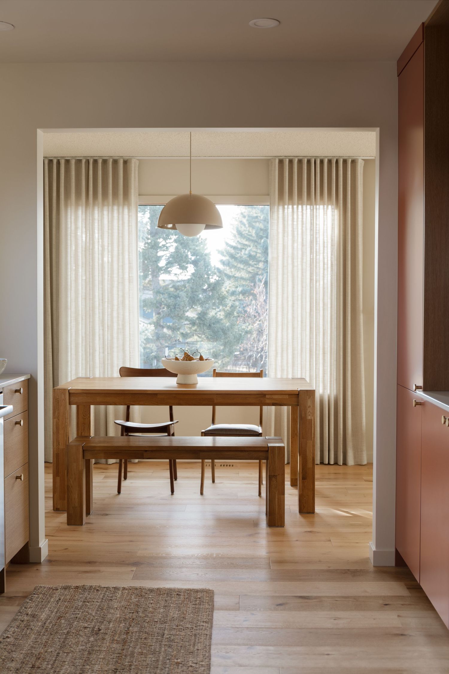 Cozy dining nook with wood table, bench seating, pendant light, and floor-to-ceiling linen curtains by Calgary photographer Rebecca Frick.