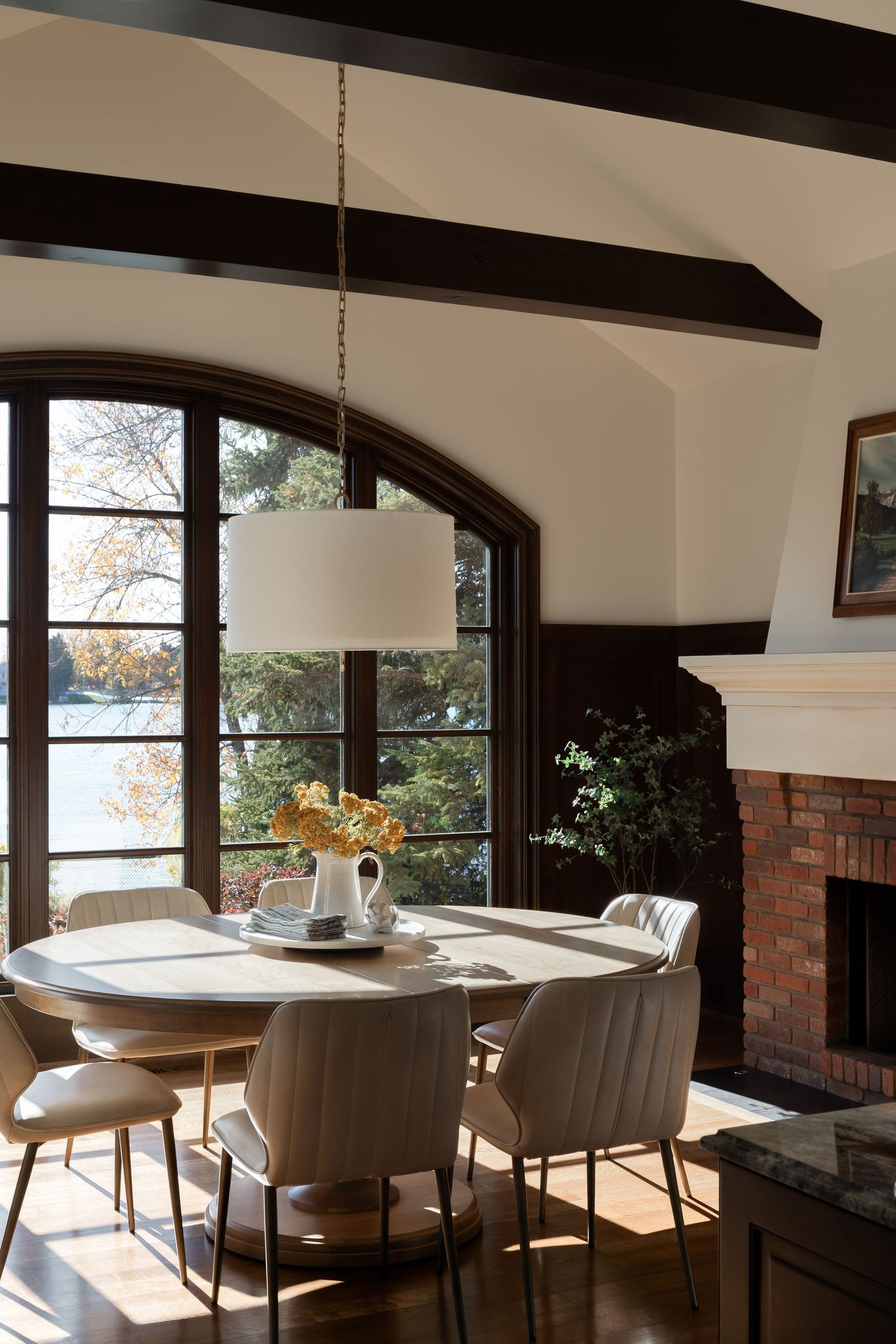Bright dining room with round white table, arched window, exposed beams, and brick fireplace by Calgary Interior photographer Rebecca Frick.