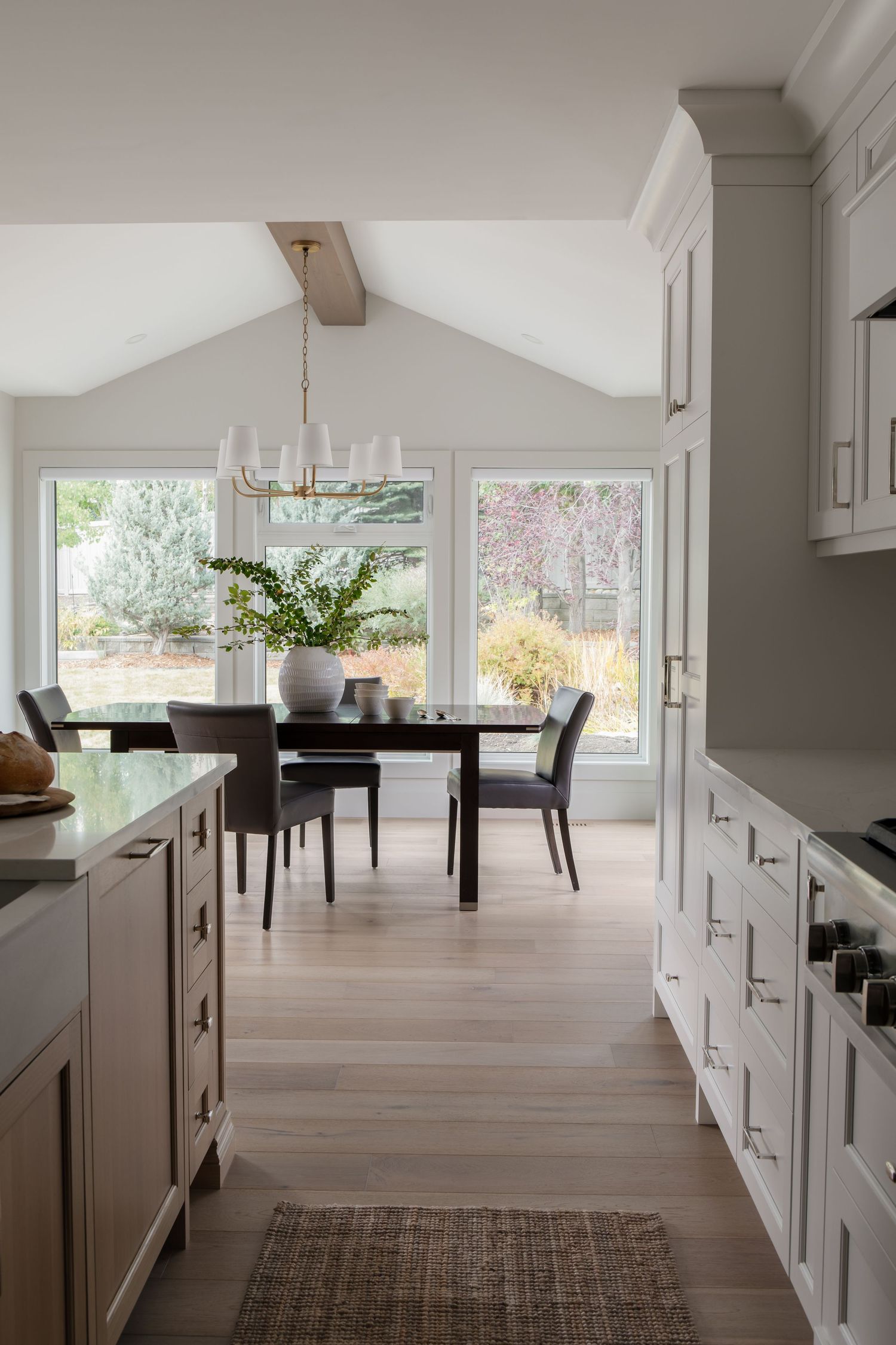 Neutral kitchen with gray cabinets, vaulted ceiling, chandelier, and sunlit dining, by Calgary Interior photographer Rebecca Frick.