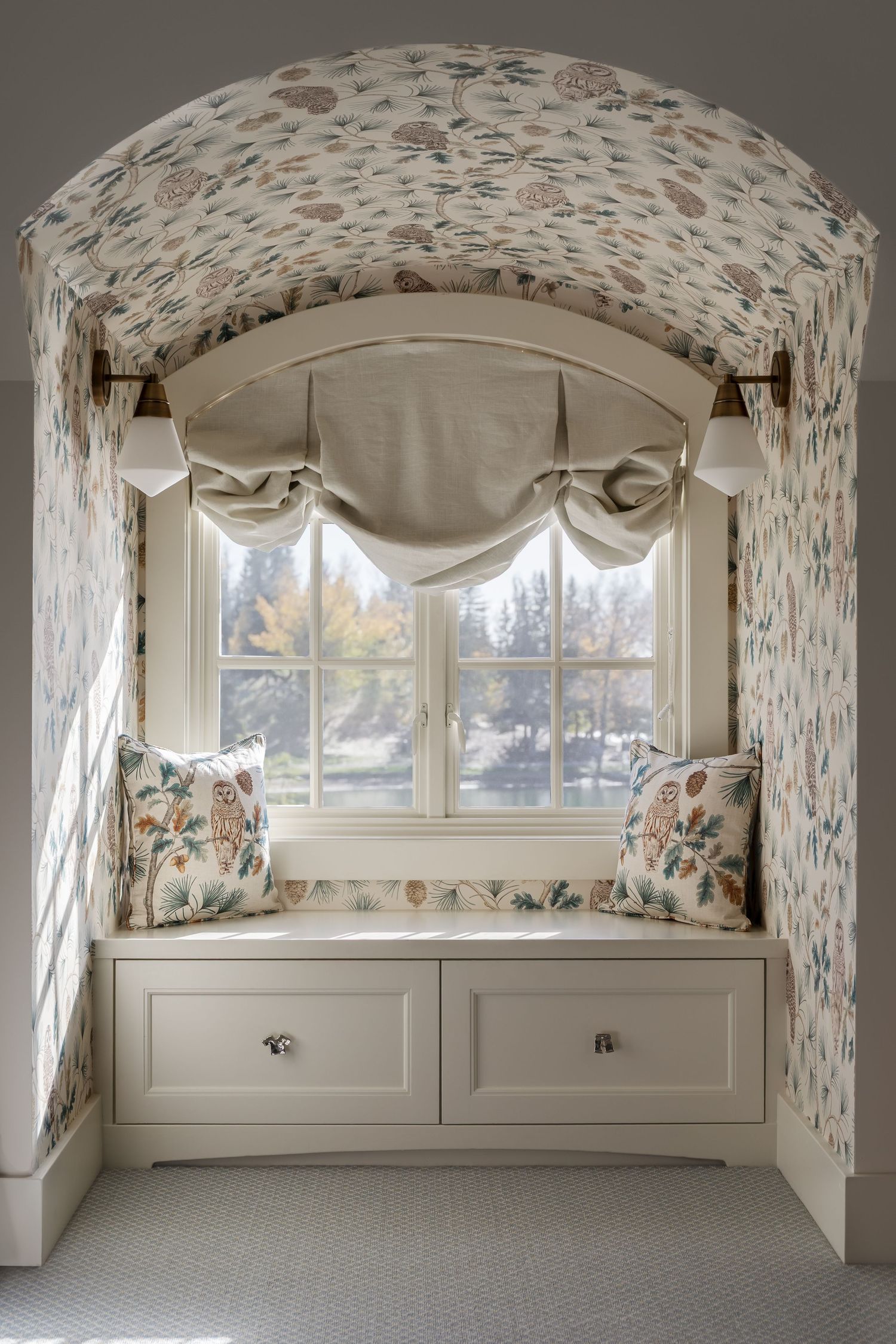Charming arched window seat nook with floral wallpaper, built-in storage, and roman shade.