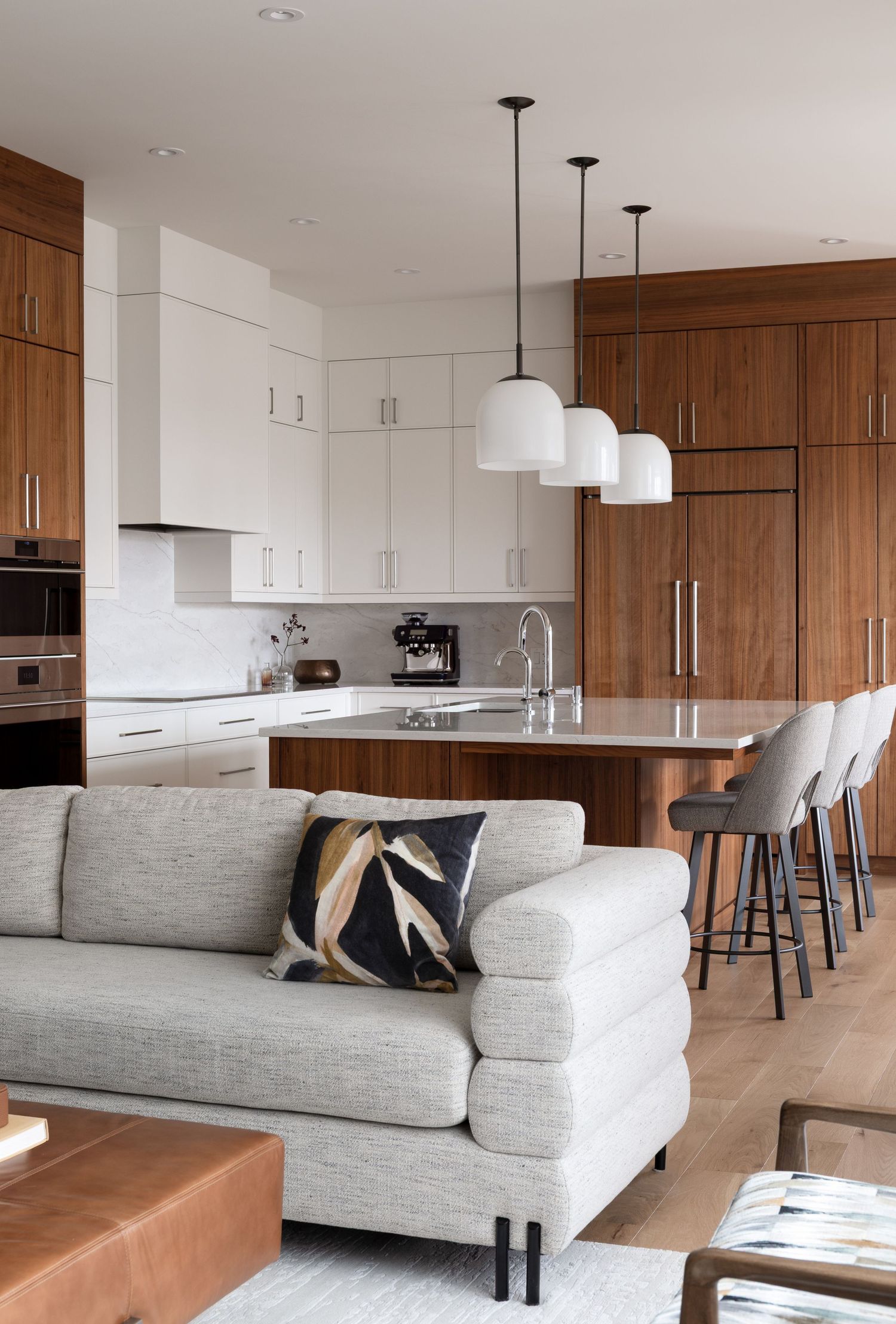 Modern open-concept kitchen and living room with walnut cabinets, white pendants, gray sofa, and marble island with bar stools.