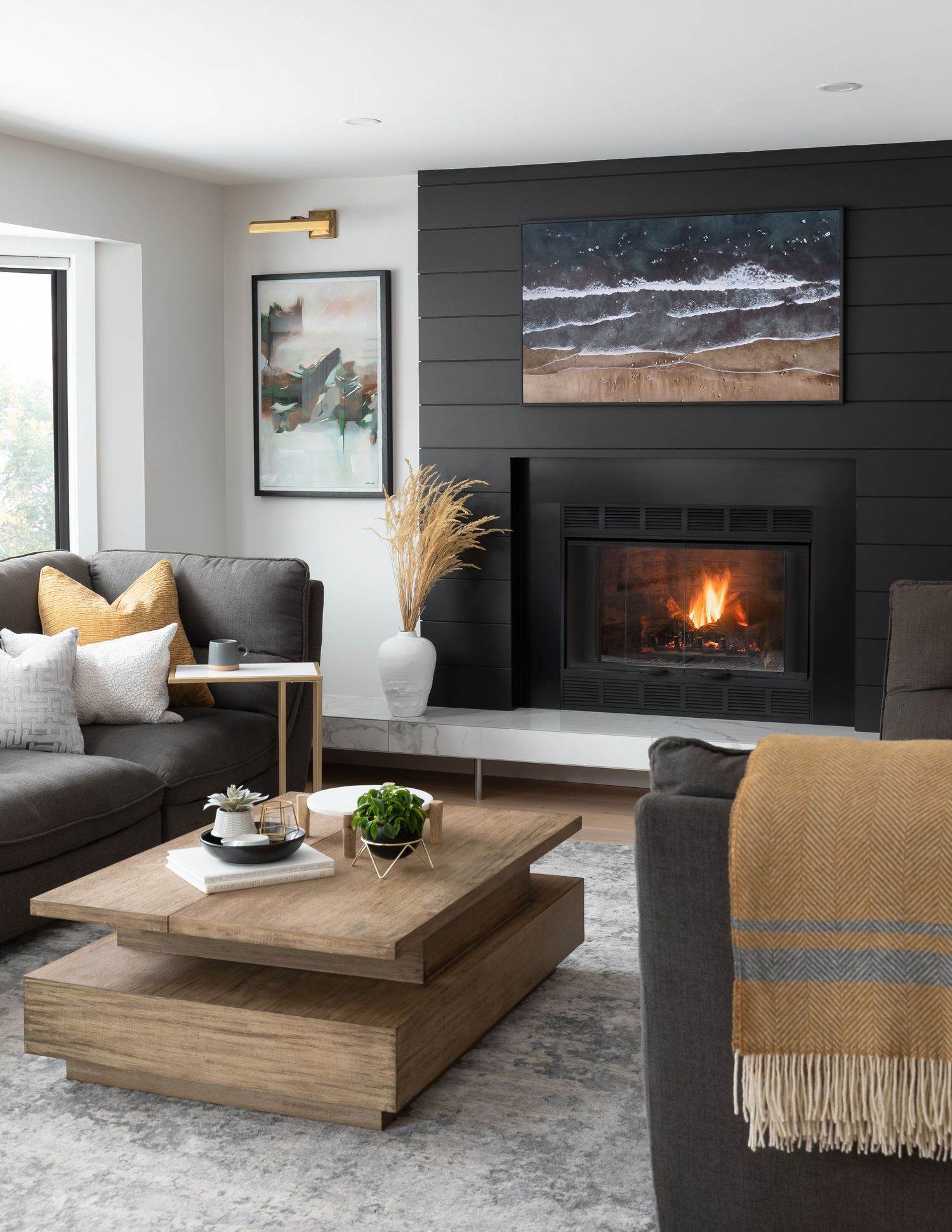 Contemporary living room with dark shiplap fireplace, gray sectional, wood coffee table, and warm mustard accents.