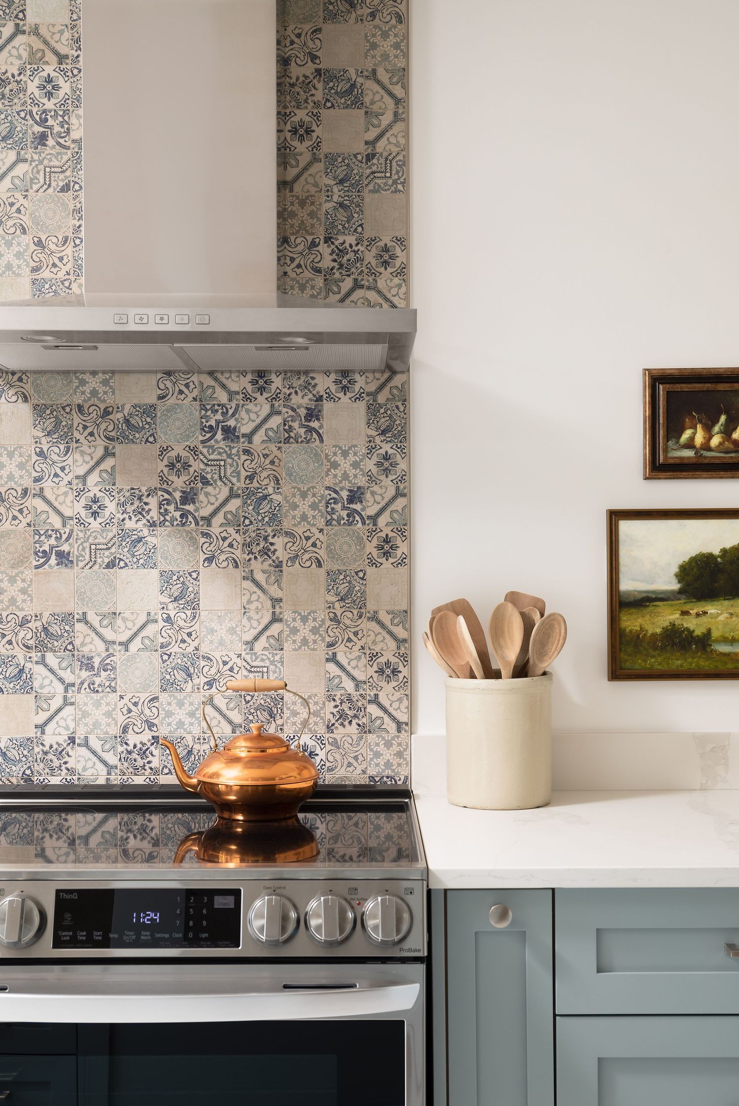Kitchen detail with patchwork tile backsplash, teal cabinets, copper kettle, and framed art.