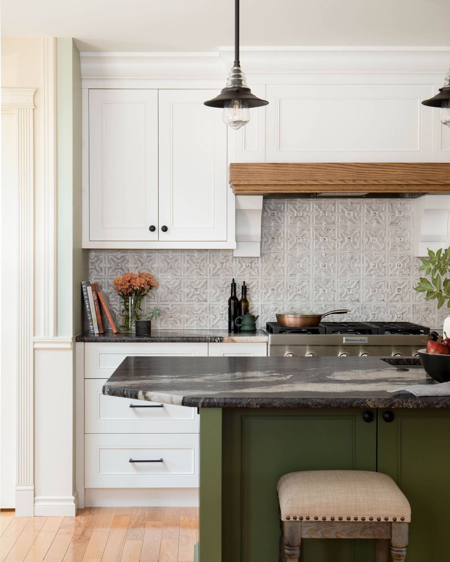 White kitchen with green island, dark stone countertops, patterned tile backsplash, and pendant lights.