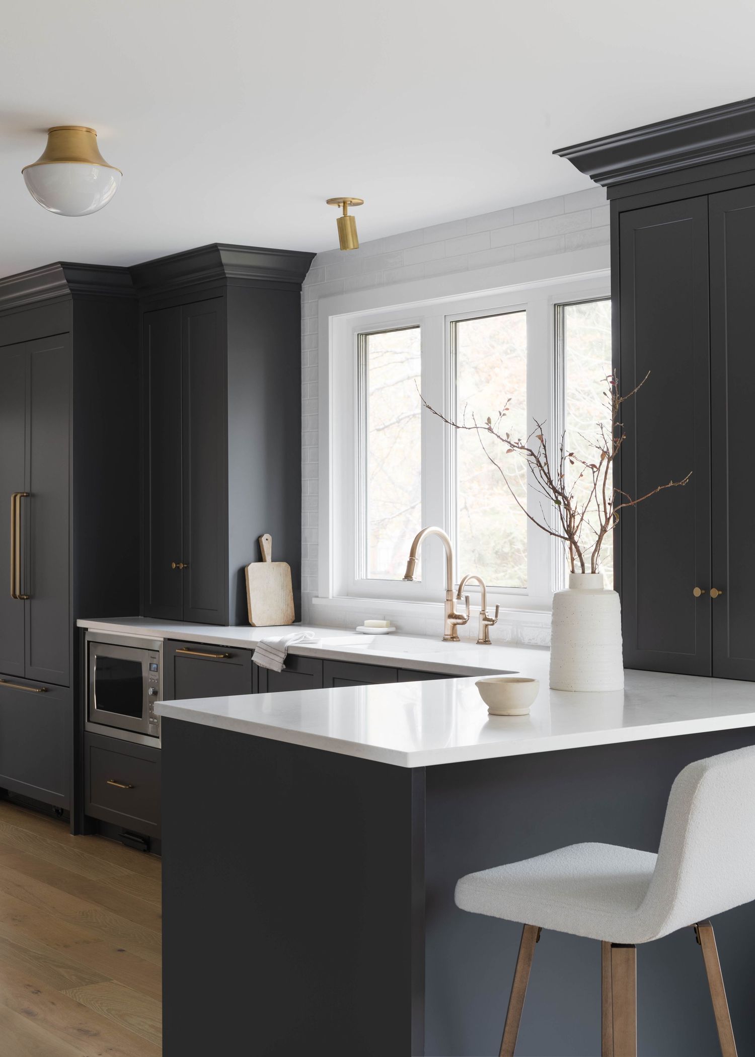 Modern dark gray kitchen with white quartz island, brass hardware, pendant light, and white bar stool.