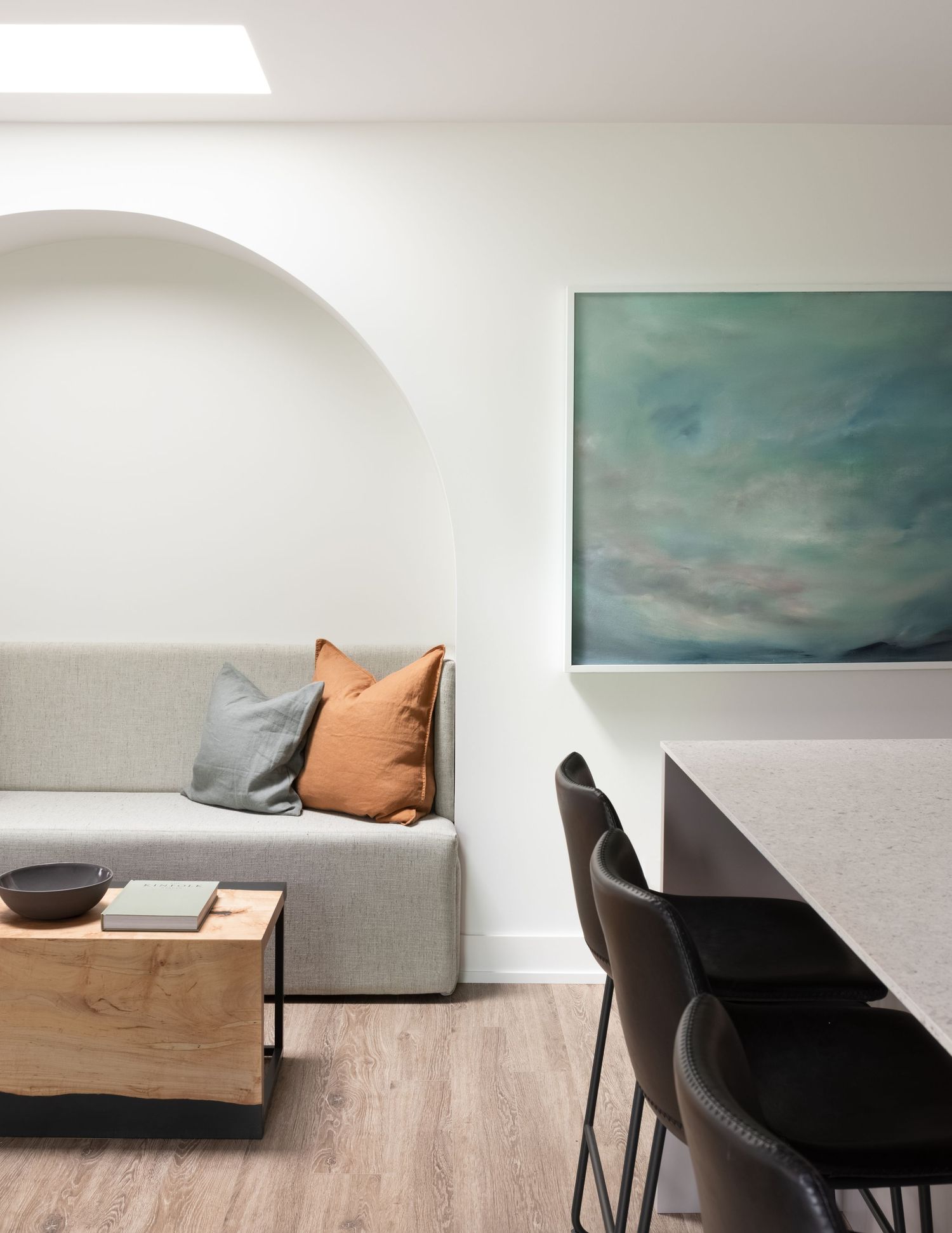Minimalist living space with arched niche sofa, wood coffee table, black dining chairs, and teal abstract wall art.