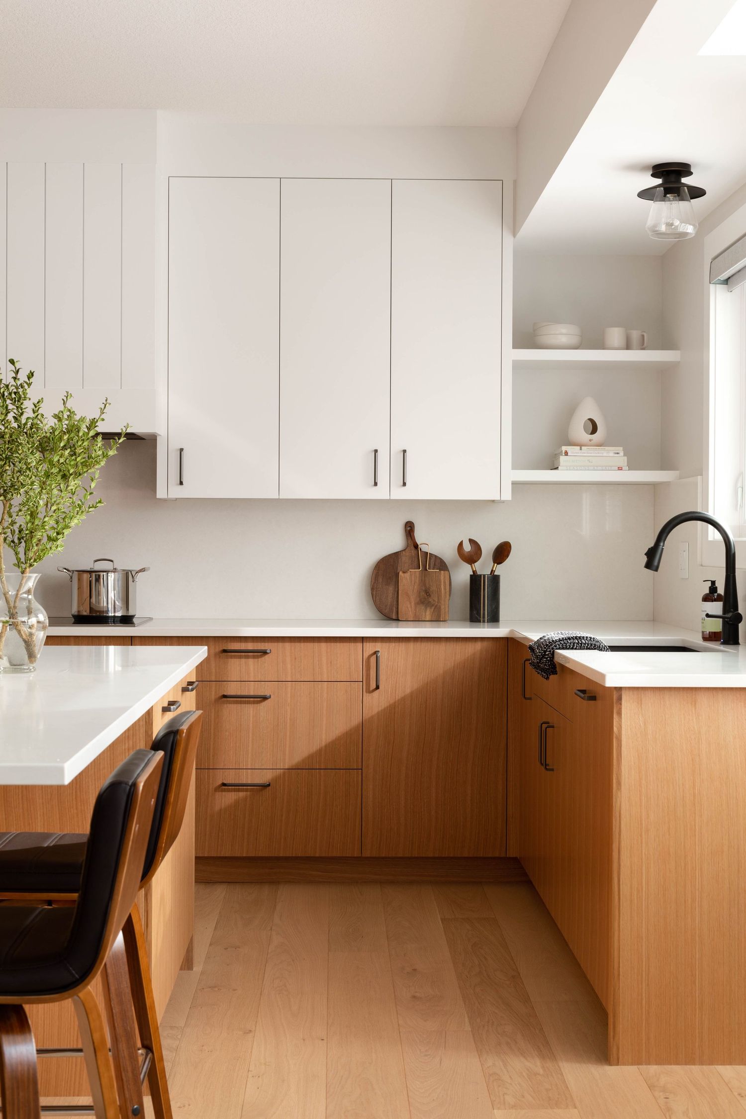 Modern kitchen with two-tone white upper cabinets and warm wood lower cabinets, white countertops, and open shelving.