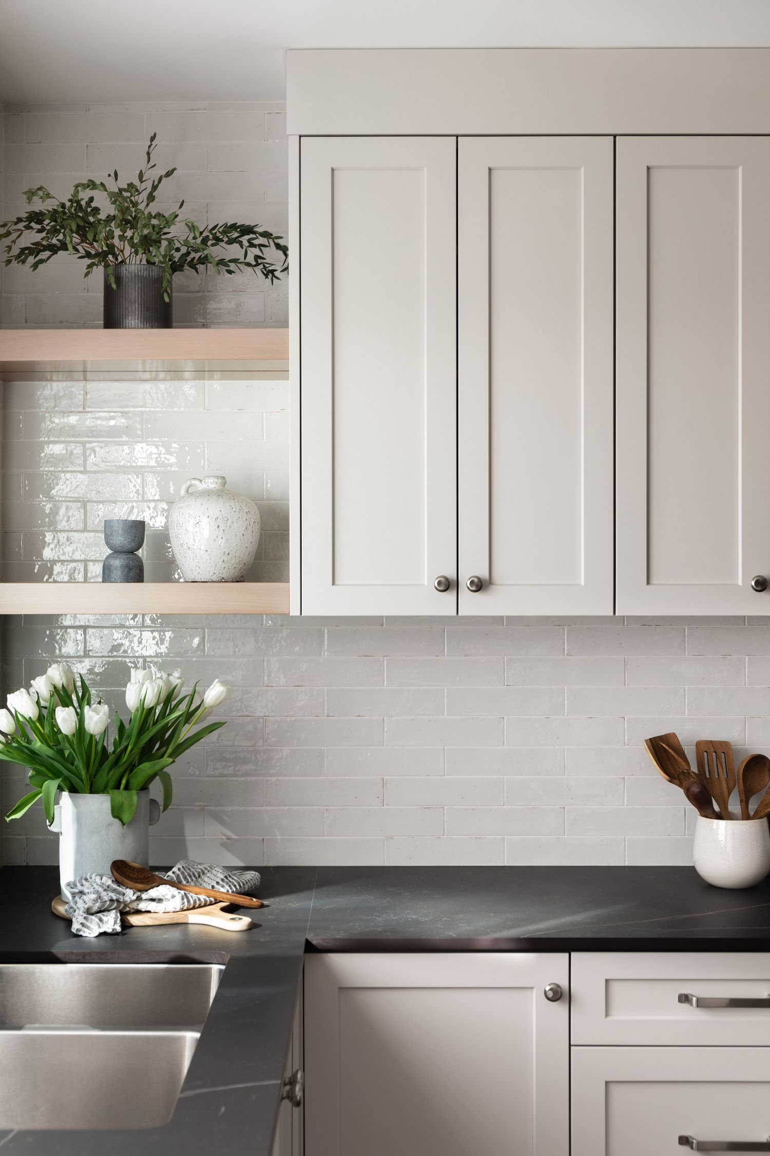 White shaker cabinets with black countertops, subway tile backsplash, and open shelving with decor.