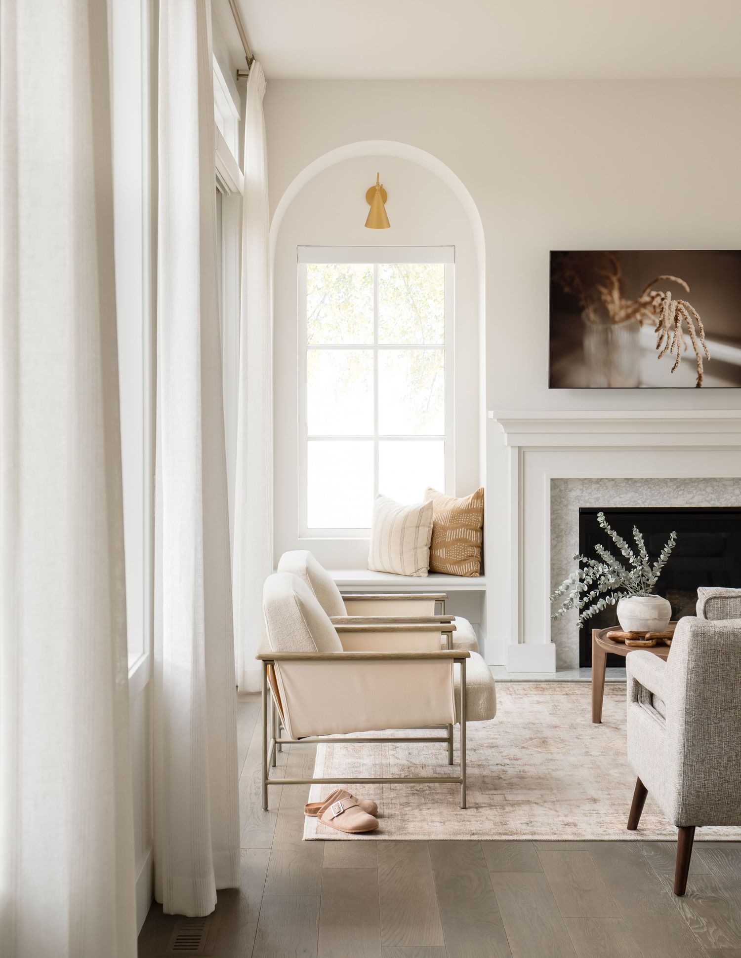 Bright living room with arched window nook, cream armchair, pink rug, and white fireplace mantel.