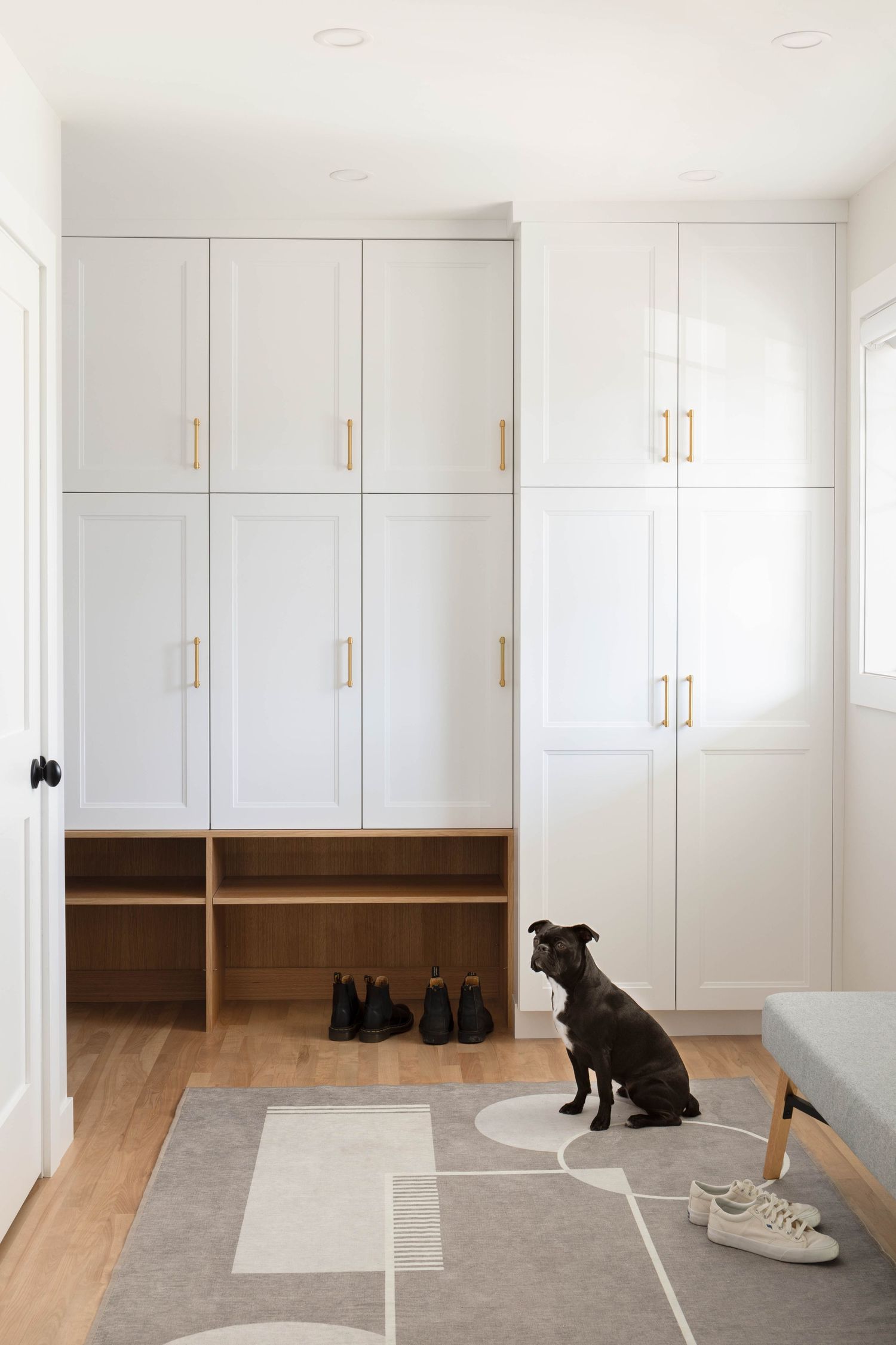White shaker mudroom cabinets with brass pulls, wood cubbies, and black French bulldog.