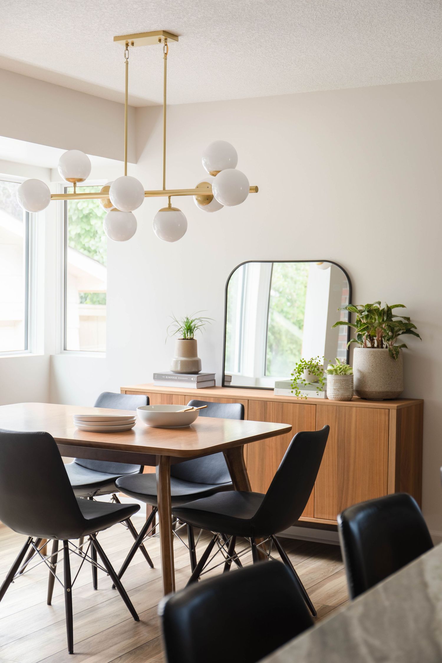 Mid-century modern dining room with brass globe chandelier, walnut sideboard, black chairs, and large window with natural light.