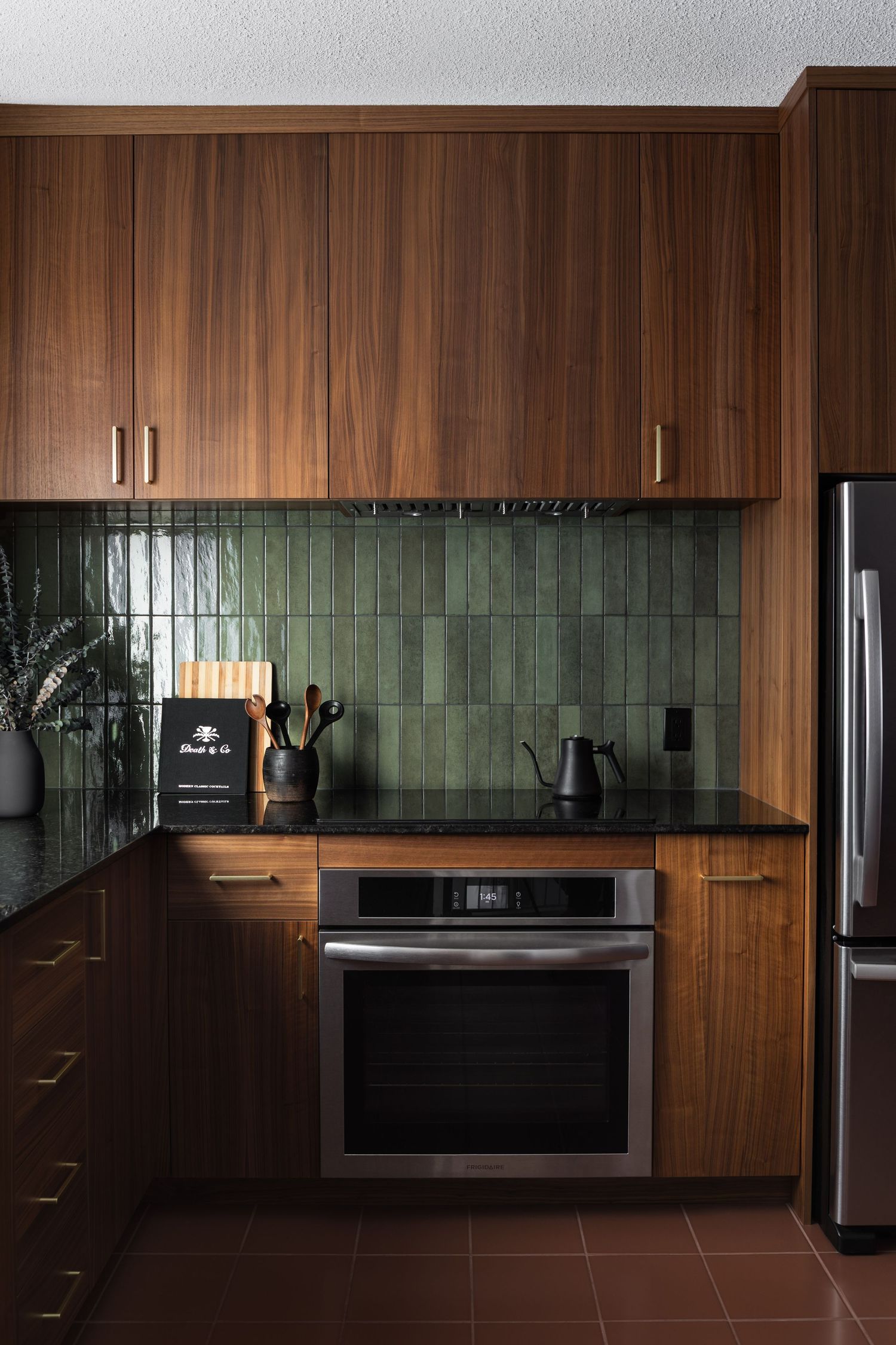 Mid-century modern kitchen with rich walnut cabinets, green zellige tile backsplash, black countertops, and stainless appliances.