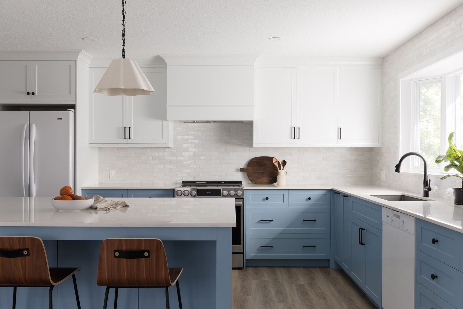 Two-tone kitchen with blue lower cabinets, white uppers, subway tile backsplash, island with wood bar stools.