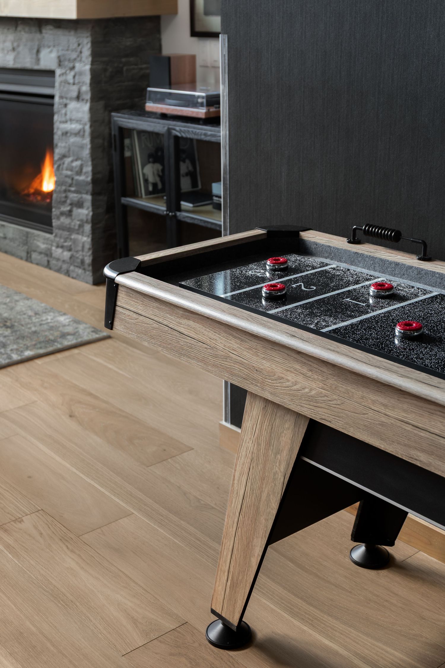 Air hockey table in a dark modern game room with stone fireplace and wood flooring.