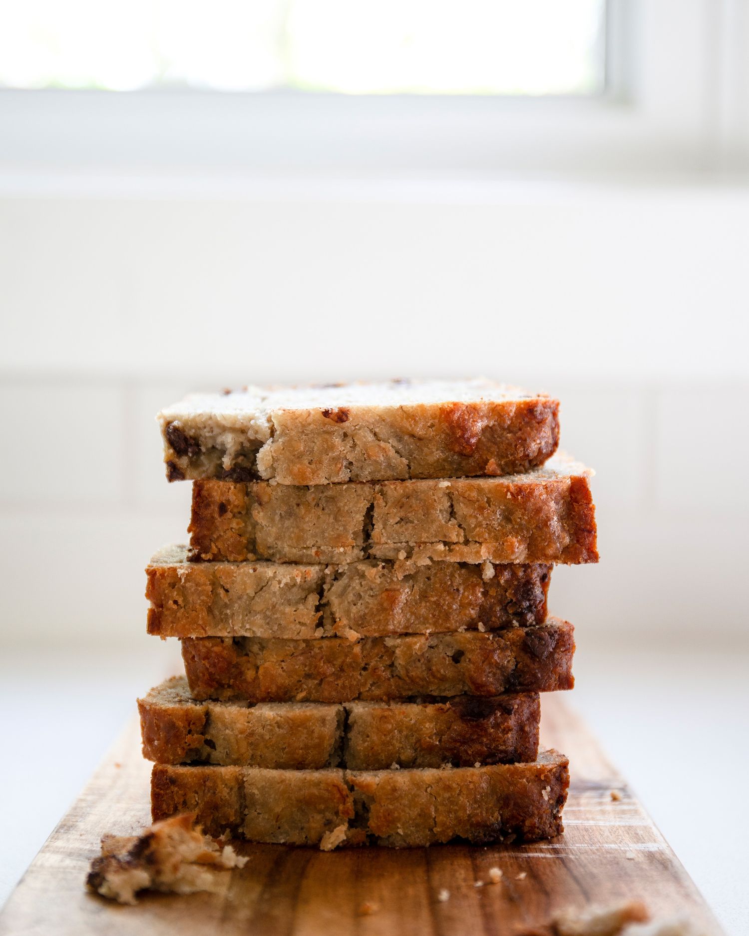 Stack of sliced banana bread with chocolate chips on a wooden cutting board.