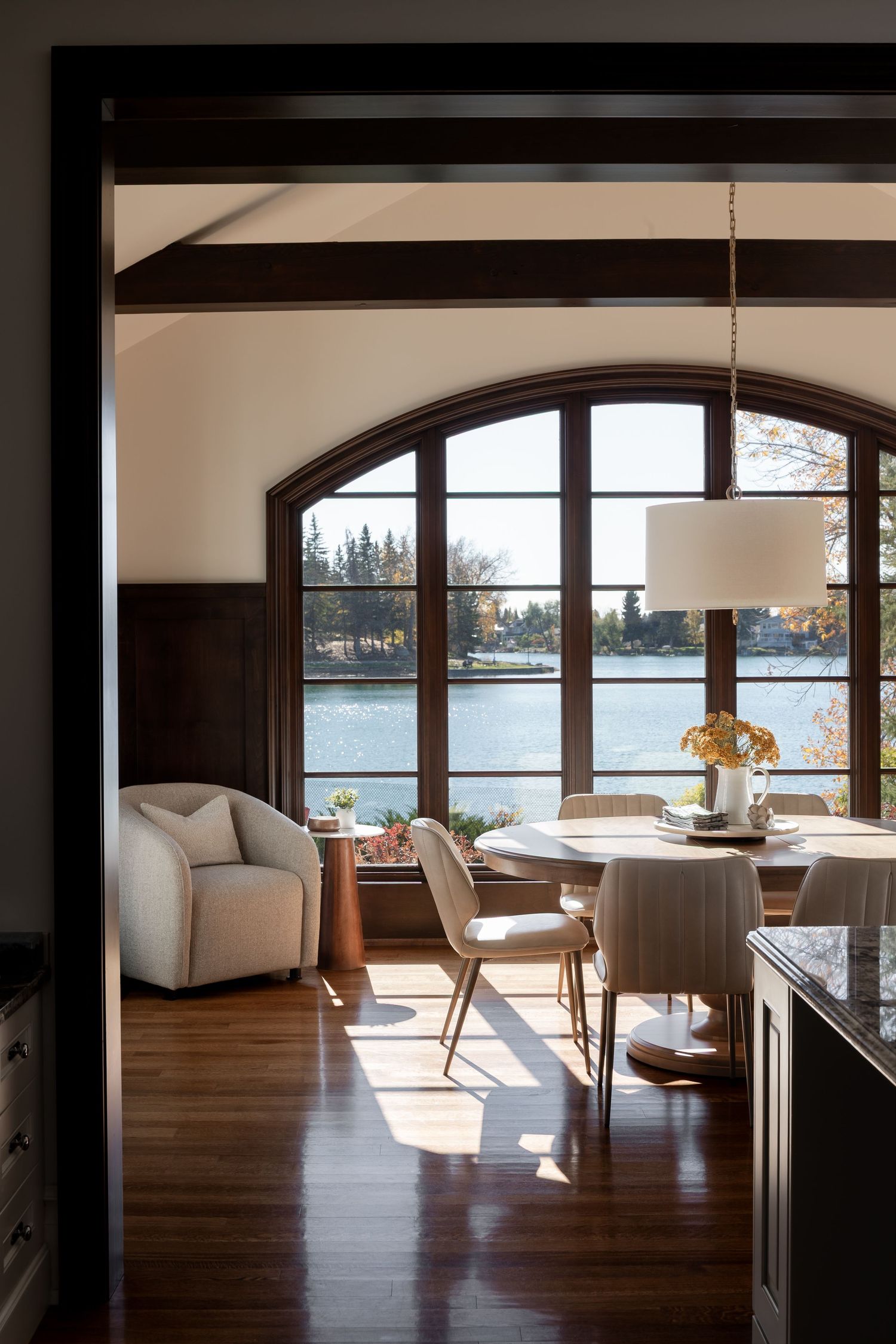 Dining nook with arched windows, round table, and exposed dark wood beams, photographed by Calgary Interior photographer Rebecca Frick.