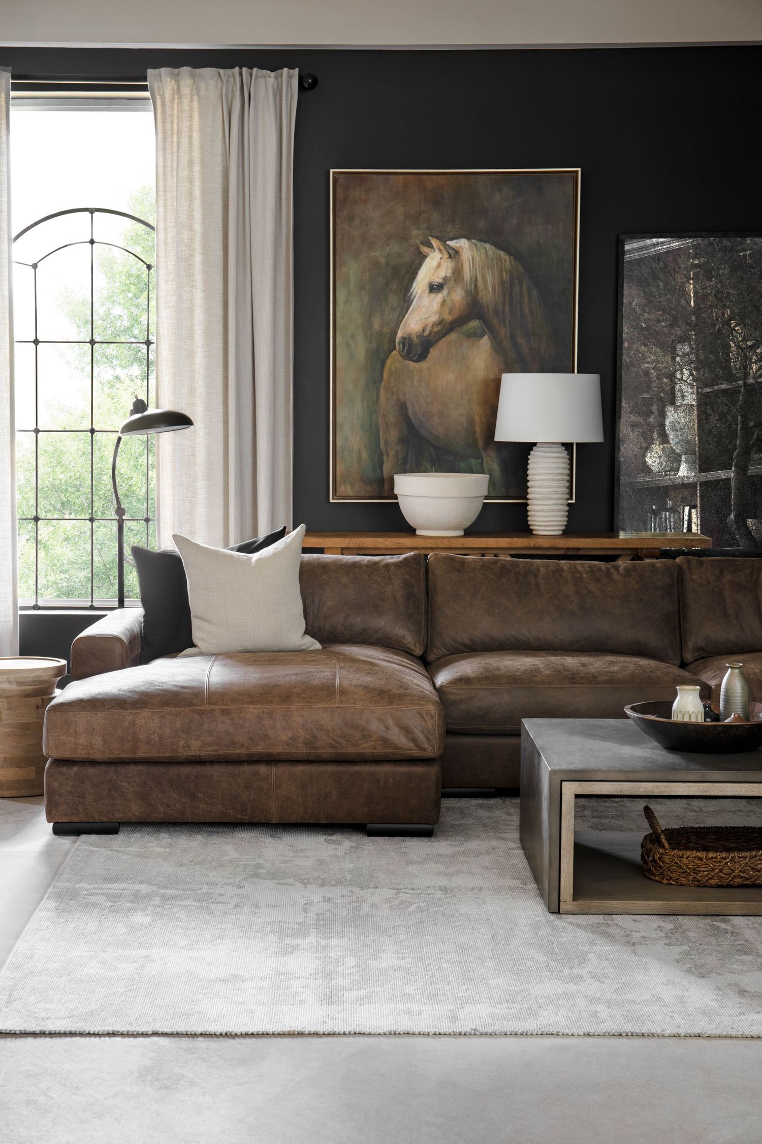 Moody living room with dark walls, brown leather sectional, and large equestrian oil painting.