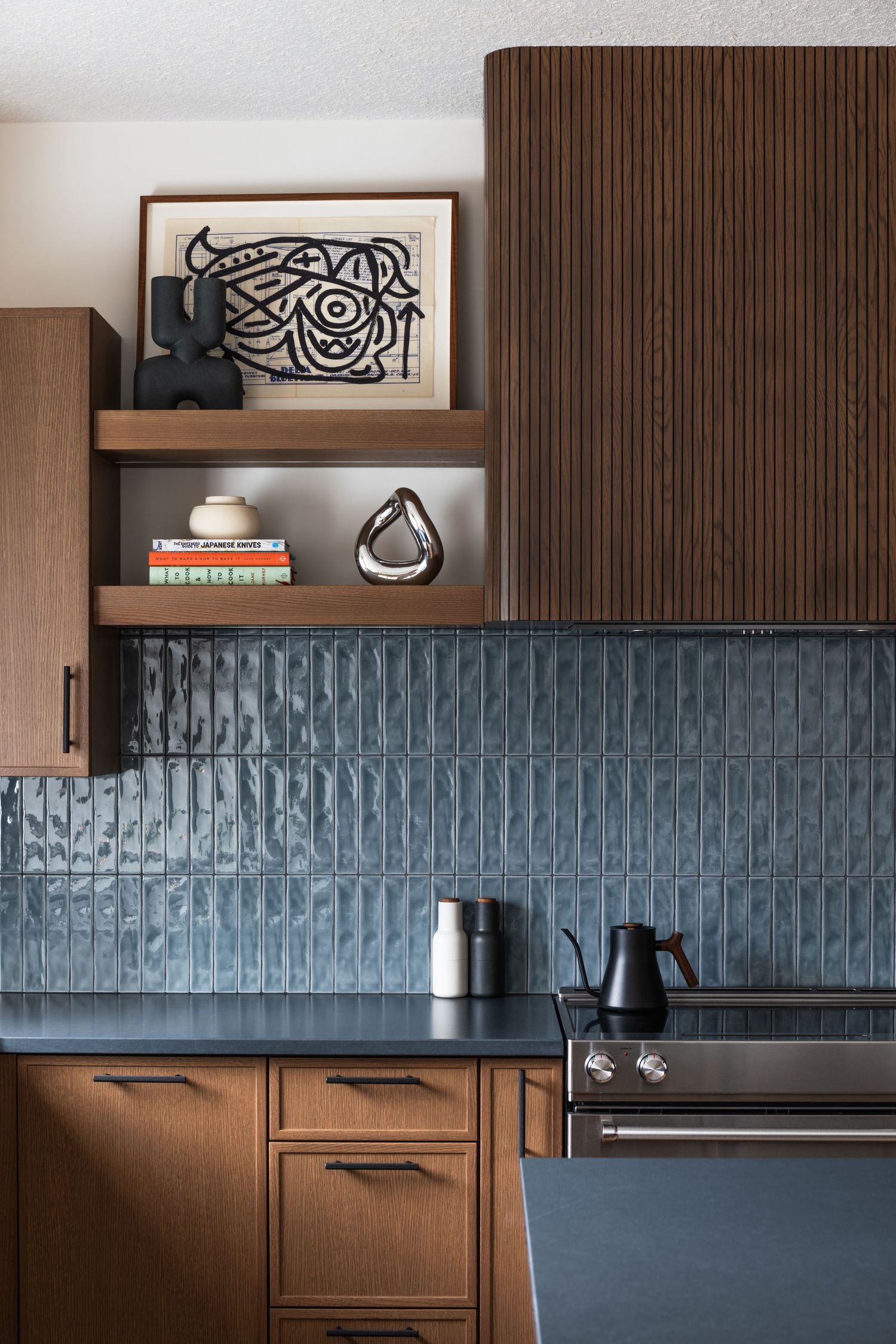 Mid-century modern kitchen with walnut cabinets, textured blue tile backsplash, open shelving, and decorative objects.