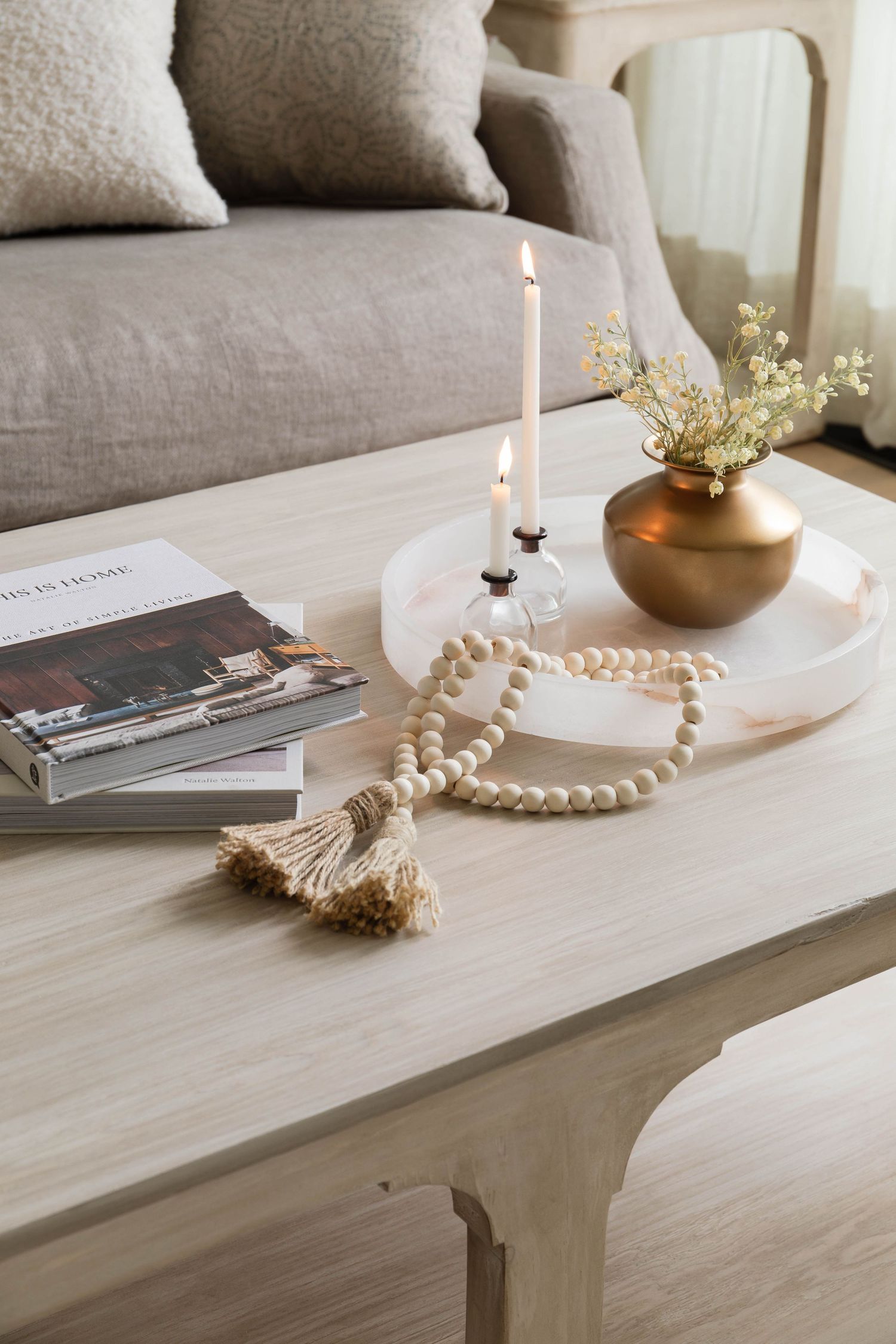 White coffee table styled with candle, brass vase, wood beads, and home decor books.