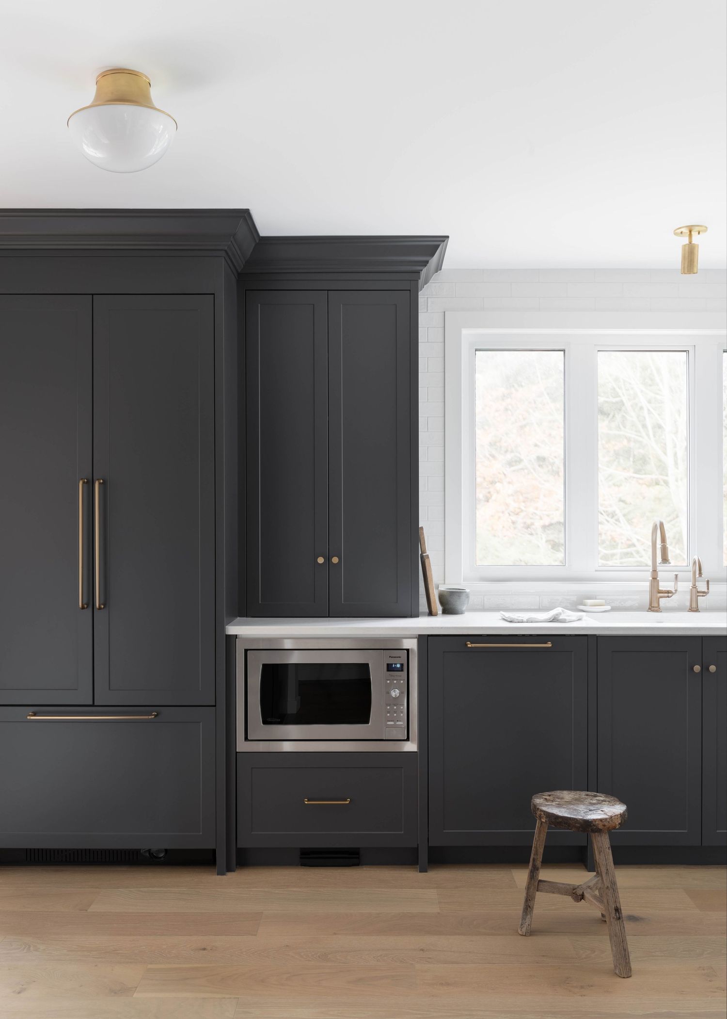 Dark charcoal kitchen with tall cabinetry, brass hardware, built-in microwave, and wood floors.