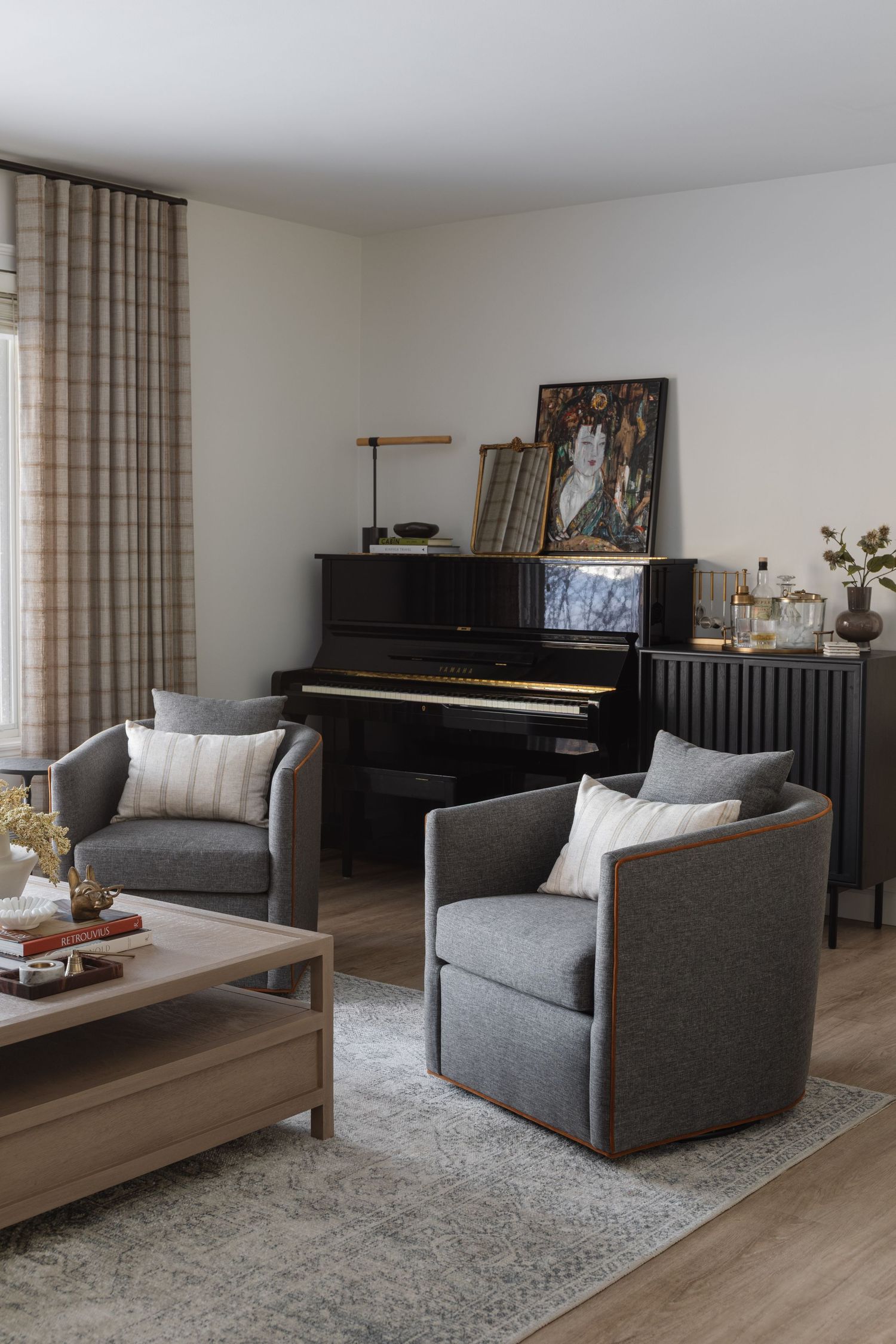 Sophisticated living room with gray swivel chairs, black upright piano, plaid curtains, and wood coffee table.